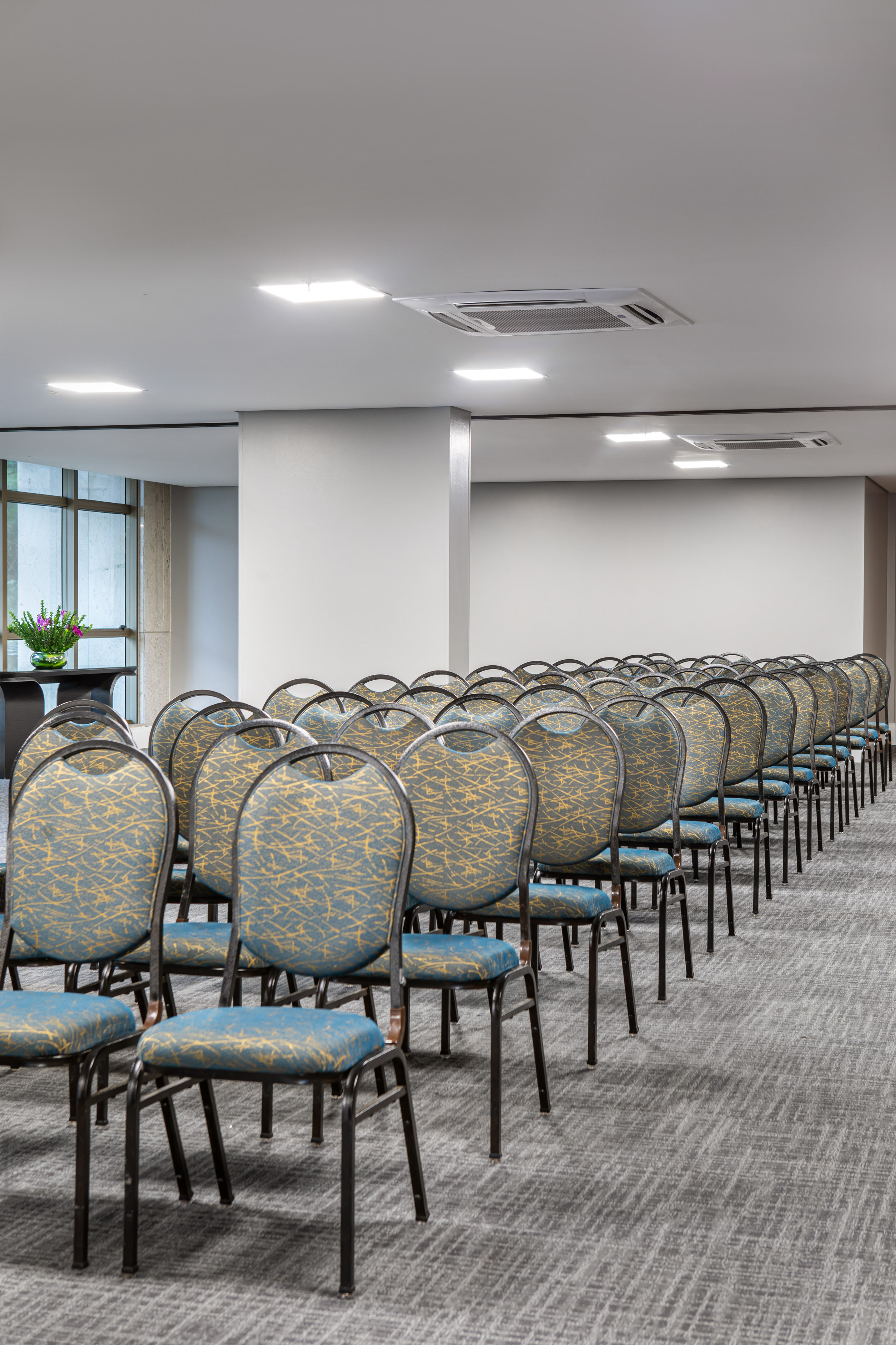 Empty conference room with rows of patterned chairs, grey carpet, and modern lights.