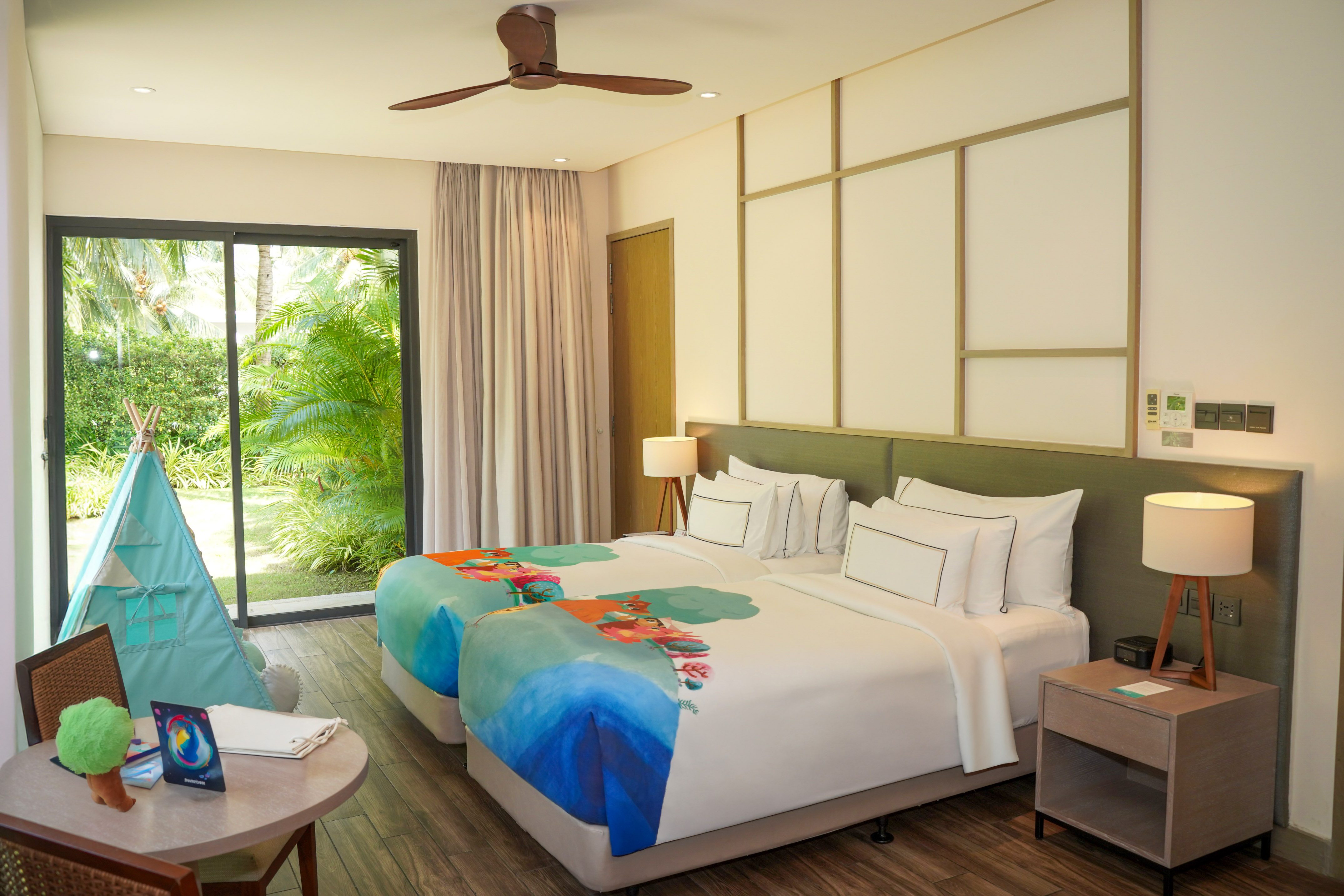 Kids' tropical resort room with colorful twin beds, play teepee, and garden view.