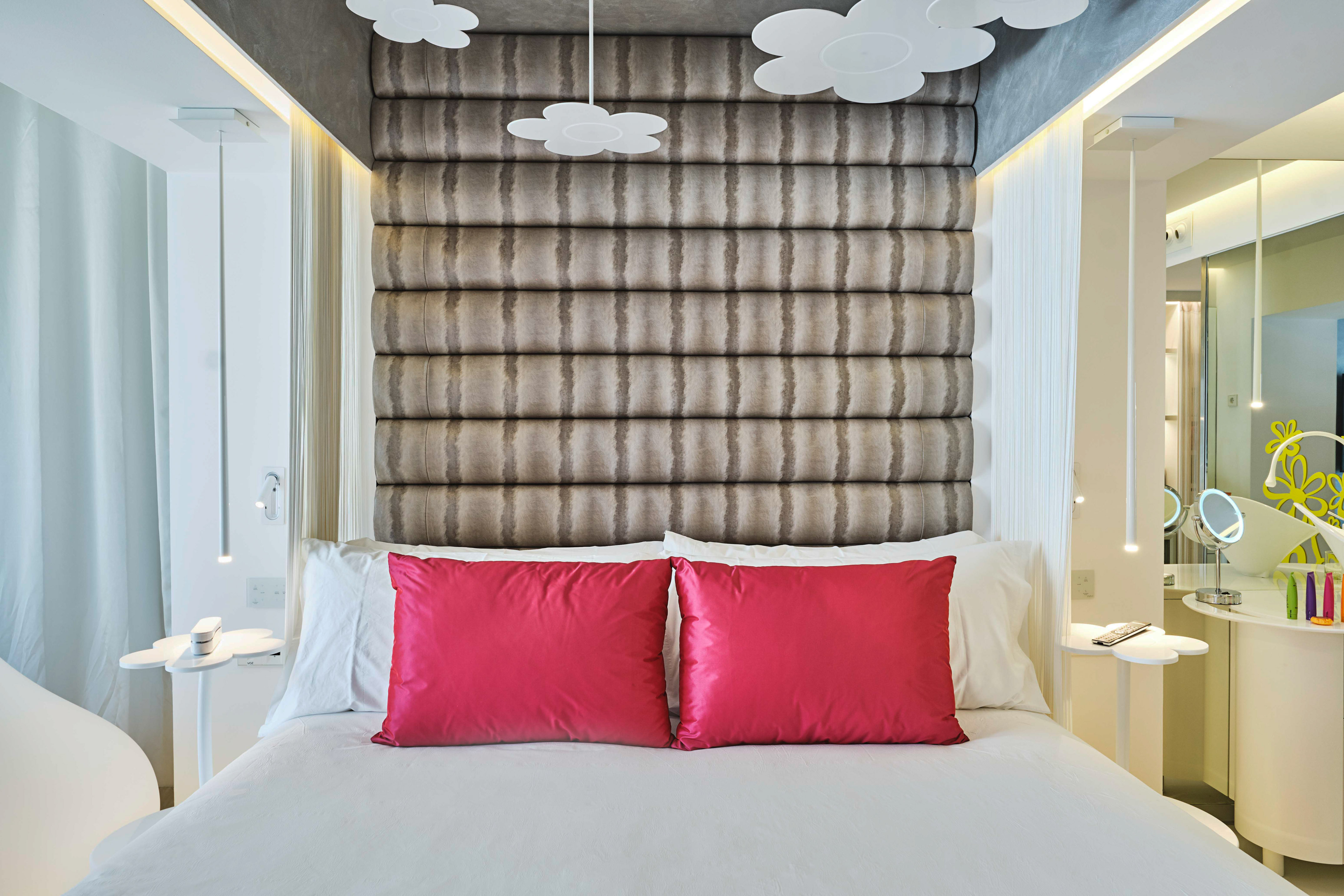 Modern hotel bedroom with tufted headboard, white bed, and vibrant pink pillows.