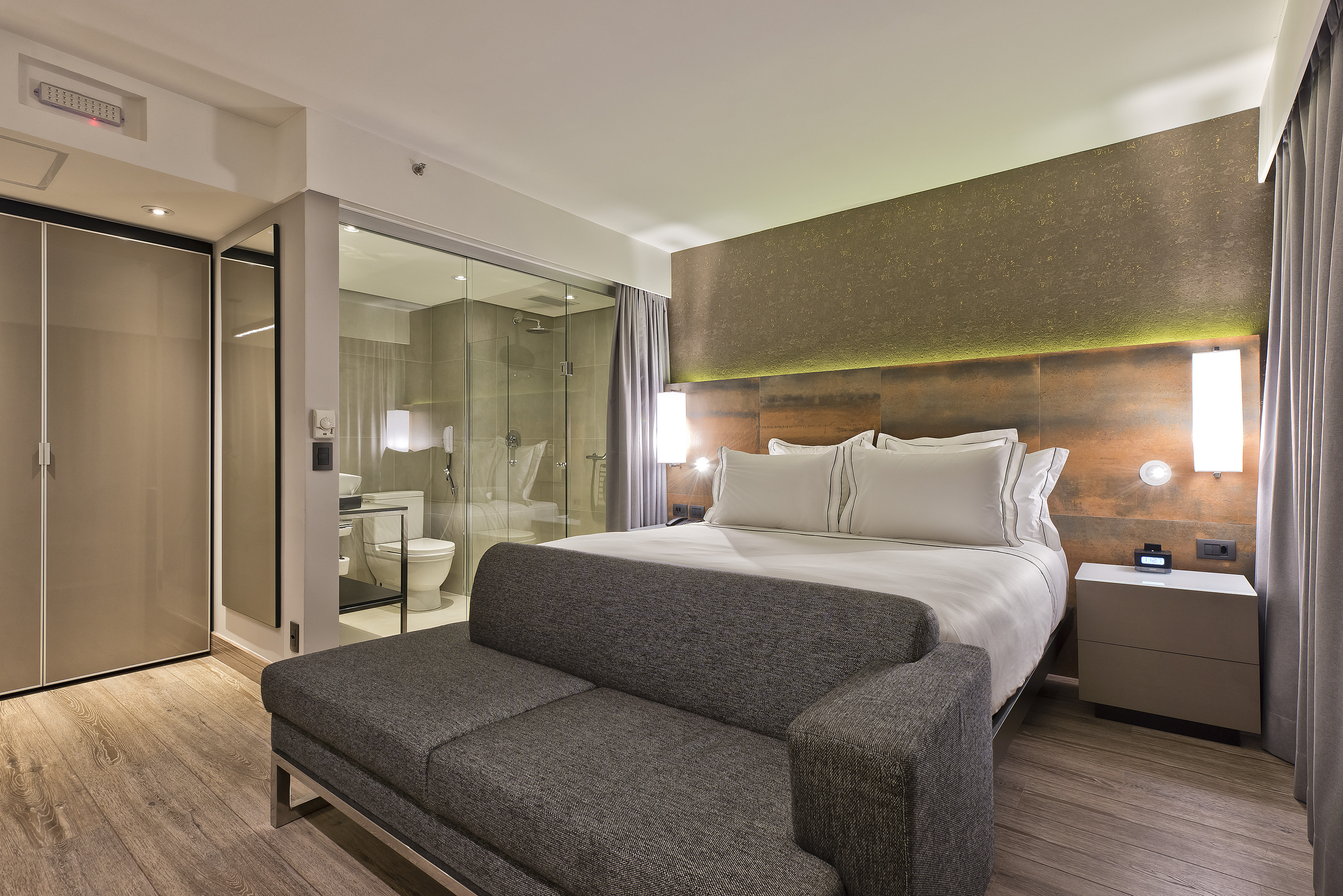 Contemporary hotel room with bed, sofa, and glass shower enclosure.