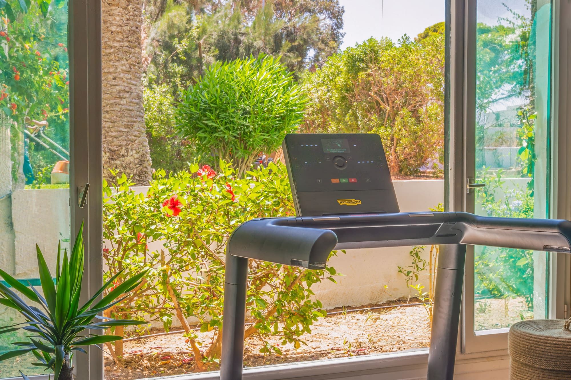 Cinta de correr Technogym frente a gran ventana con vista a jardín tropical.