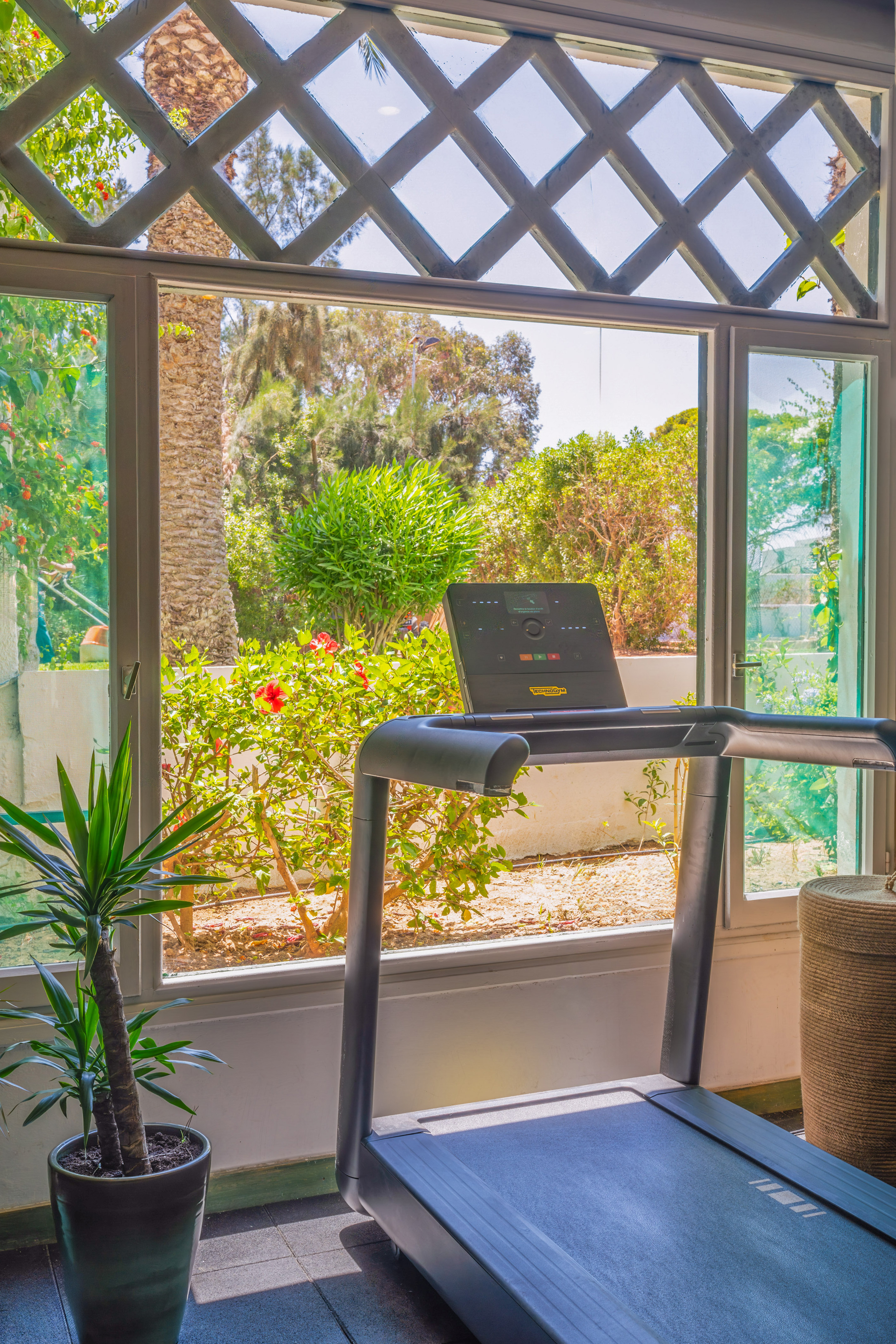 Cinta de correr Technogym frente a gran ventana con vista a jardín tropical.