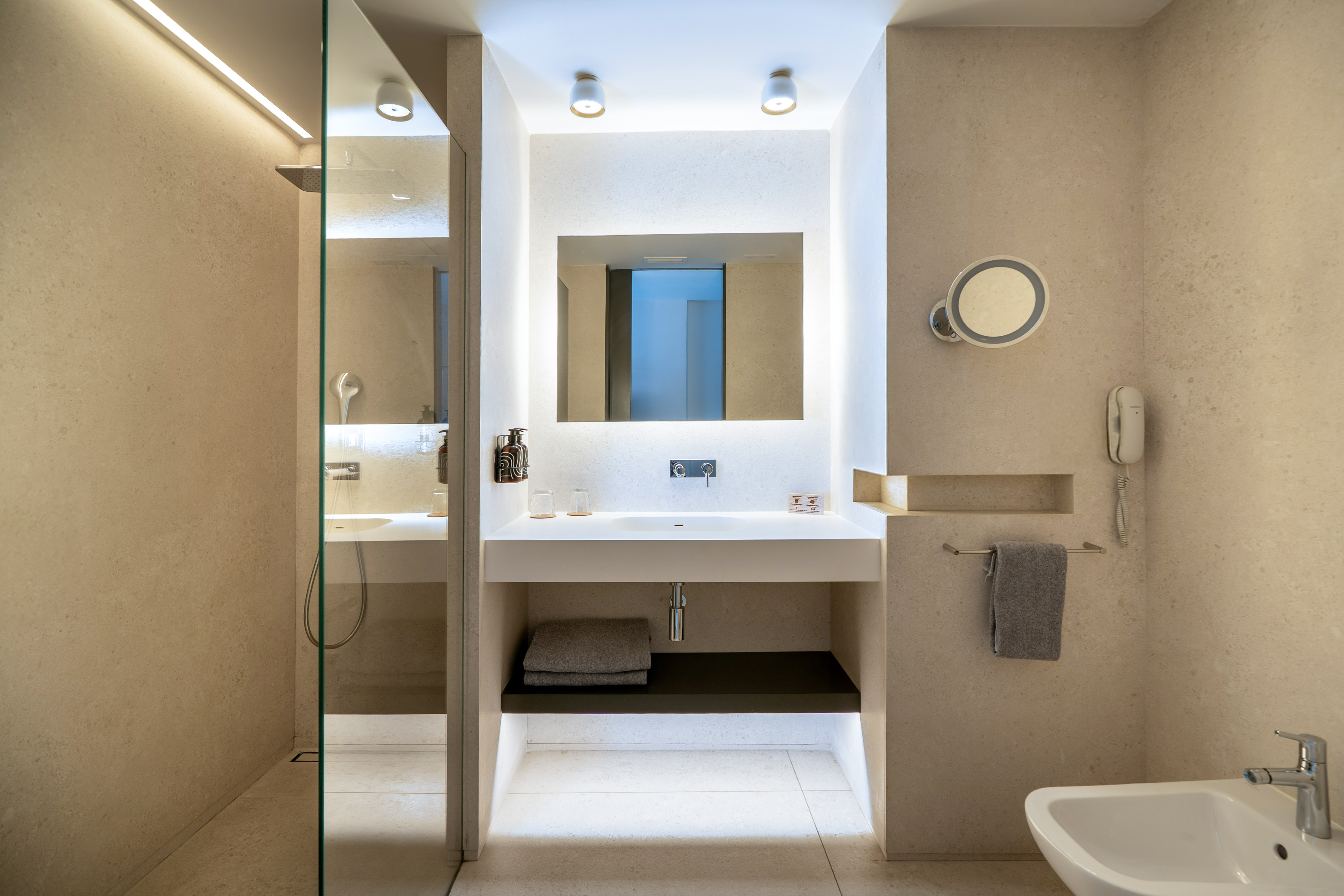 Modern minimalist bathroom with glass shower, lighted mirror, sink, bidet.