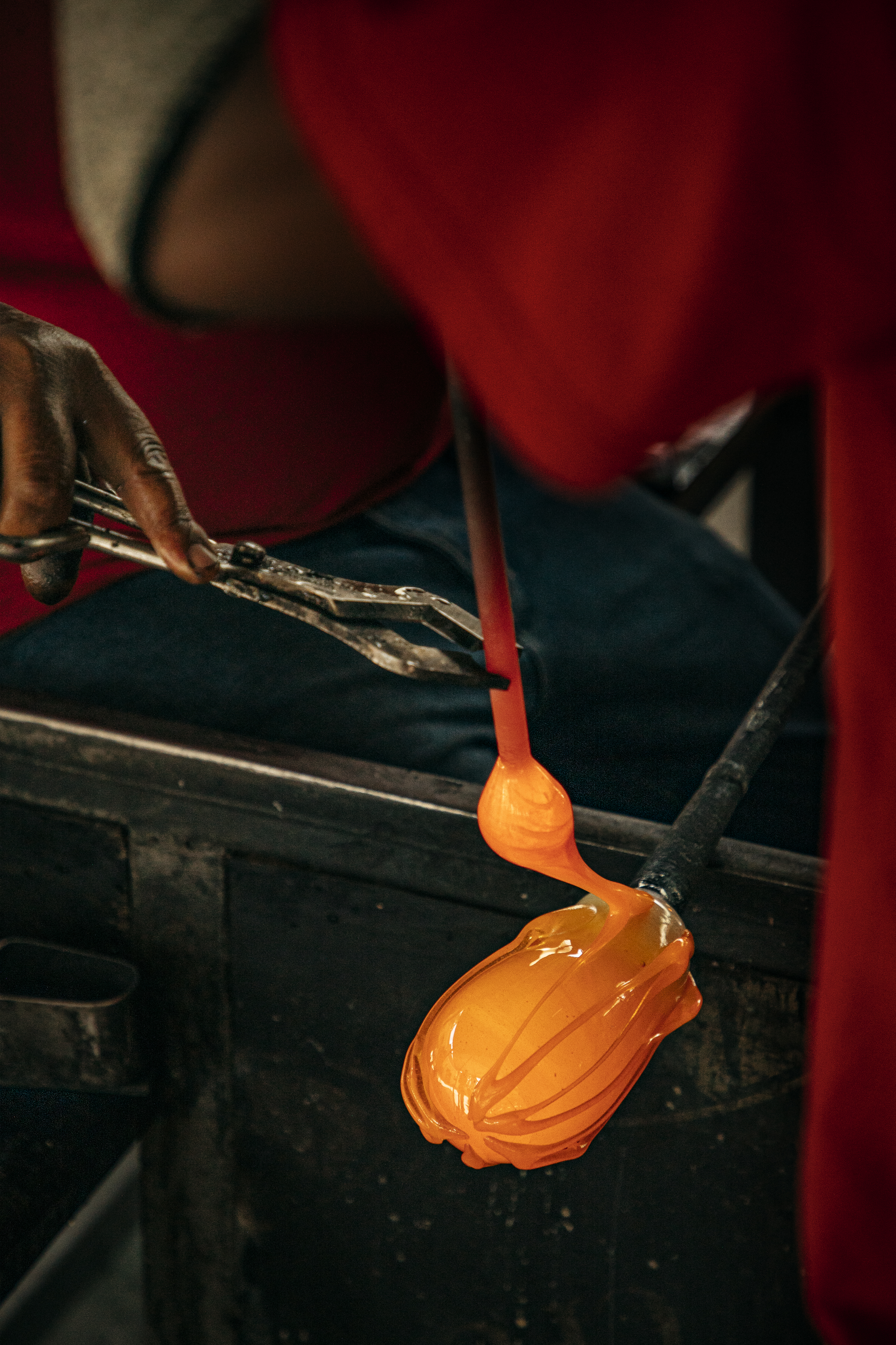 Close-up of glassblower shaping glowing orange molten glass with tongs.