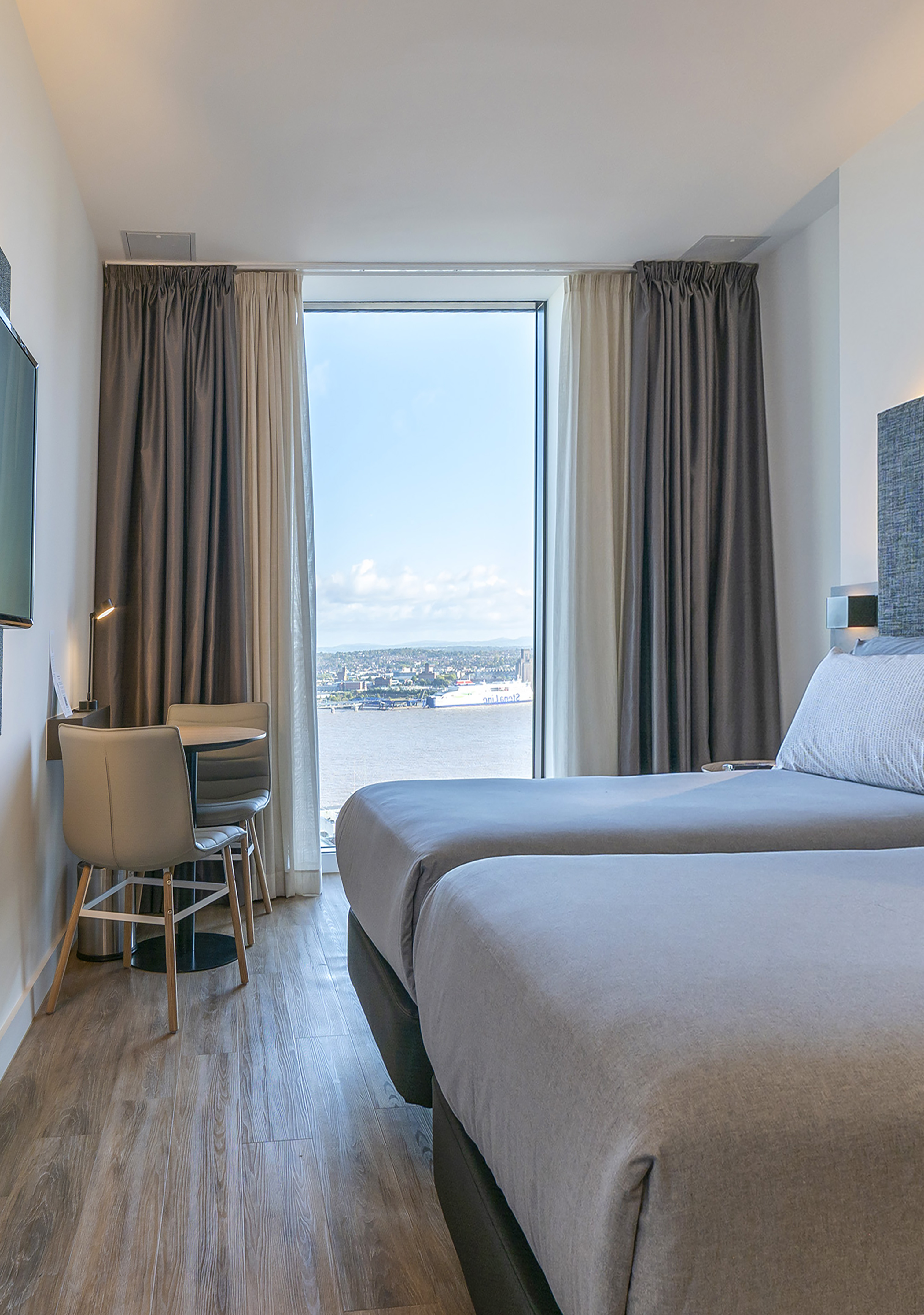 Bright twin hotel room with work desk and panoramic city river view.