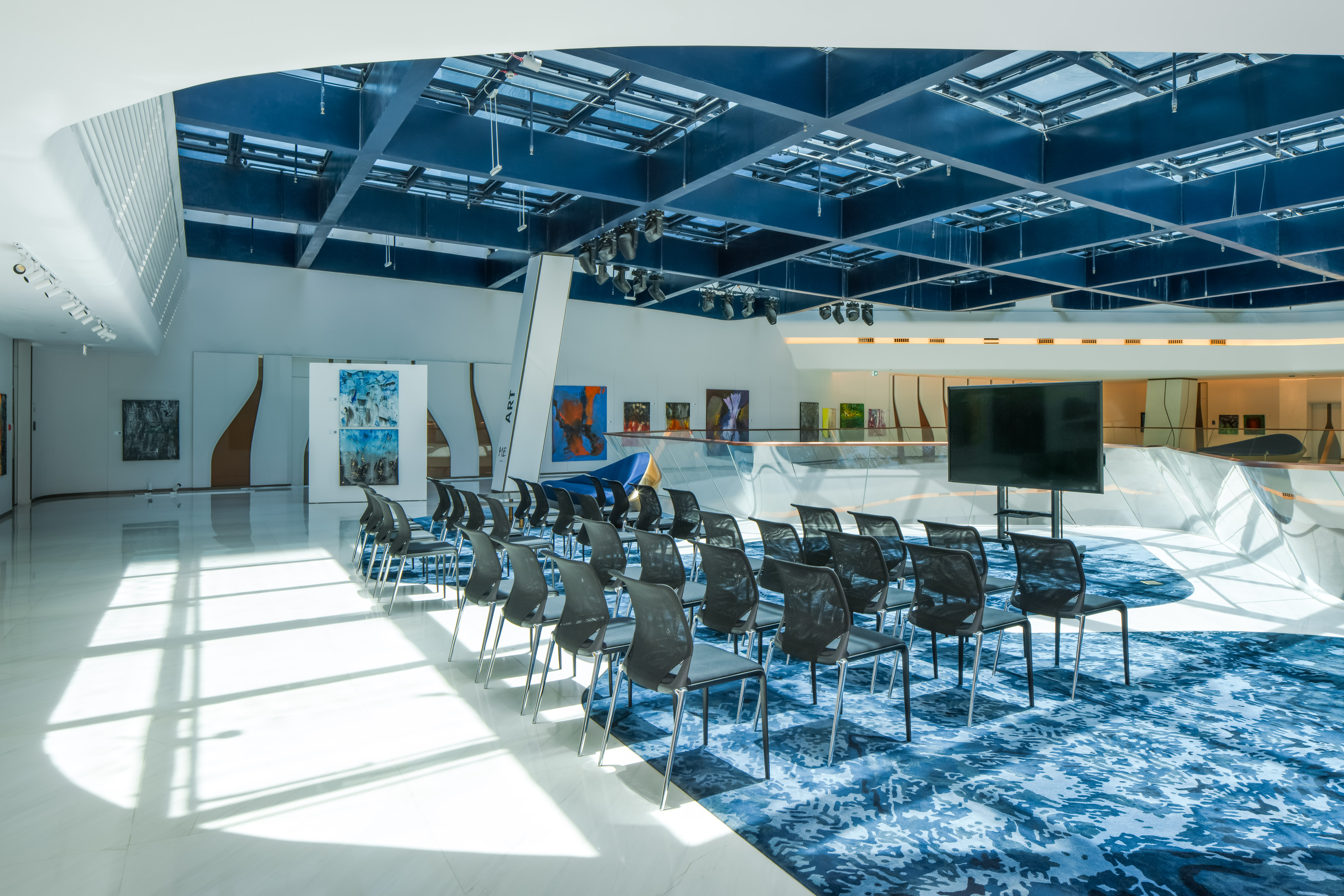 Modern event space with blue ceiling, presentation screen, patterned carpet, and art.