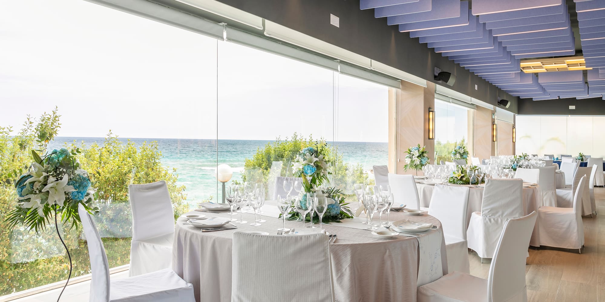 a room with tables and chairs with white chairs and a view of the ocean