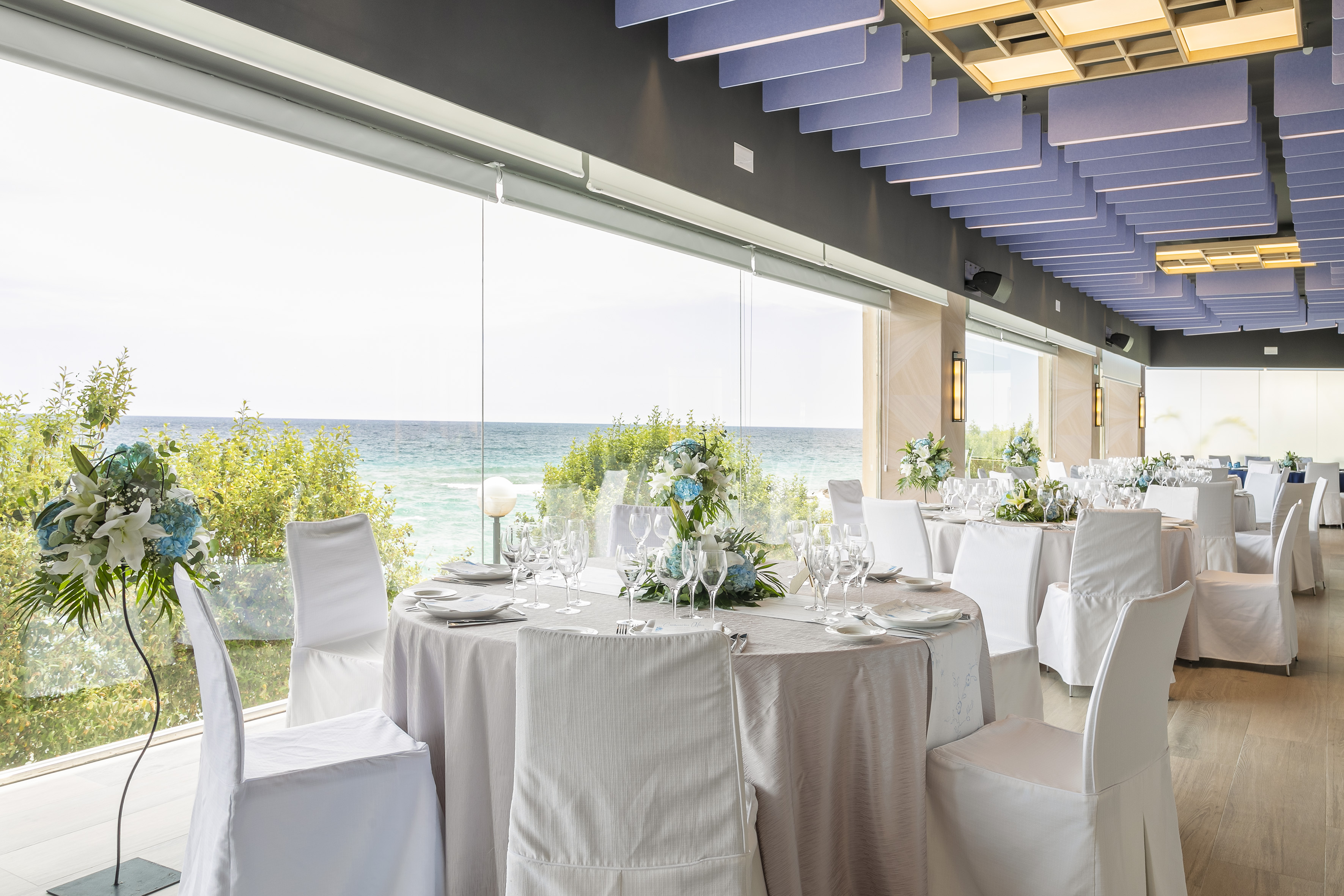 a room with tables and chairs with white chairs and a view of the ocean