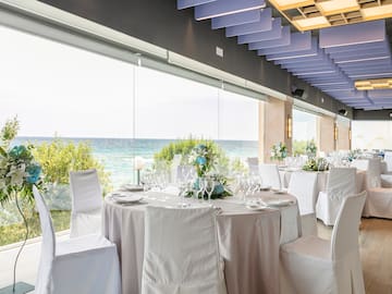 a room with tables and chairs with white chairs and a view of the ocean