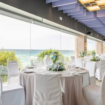 a room with tables and chairs with white chairs and a view of the ocean