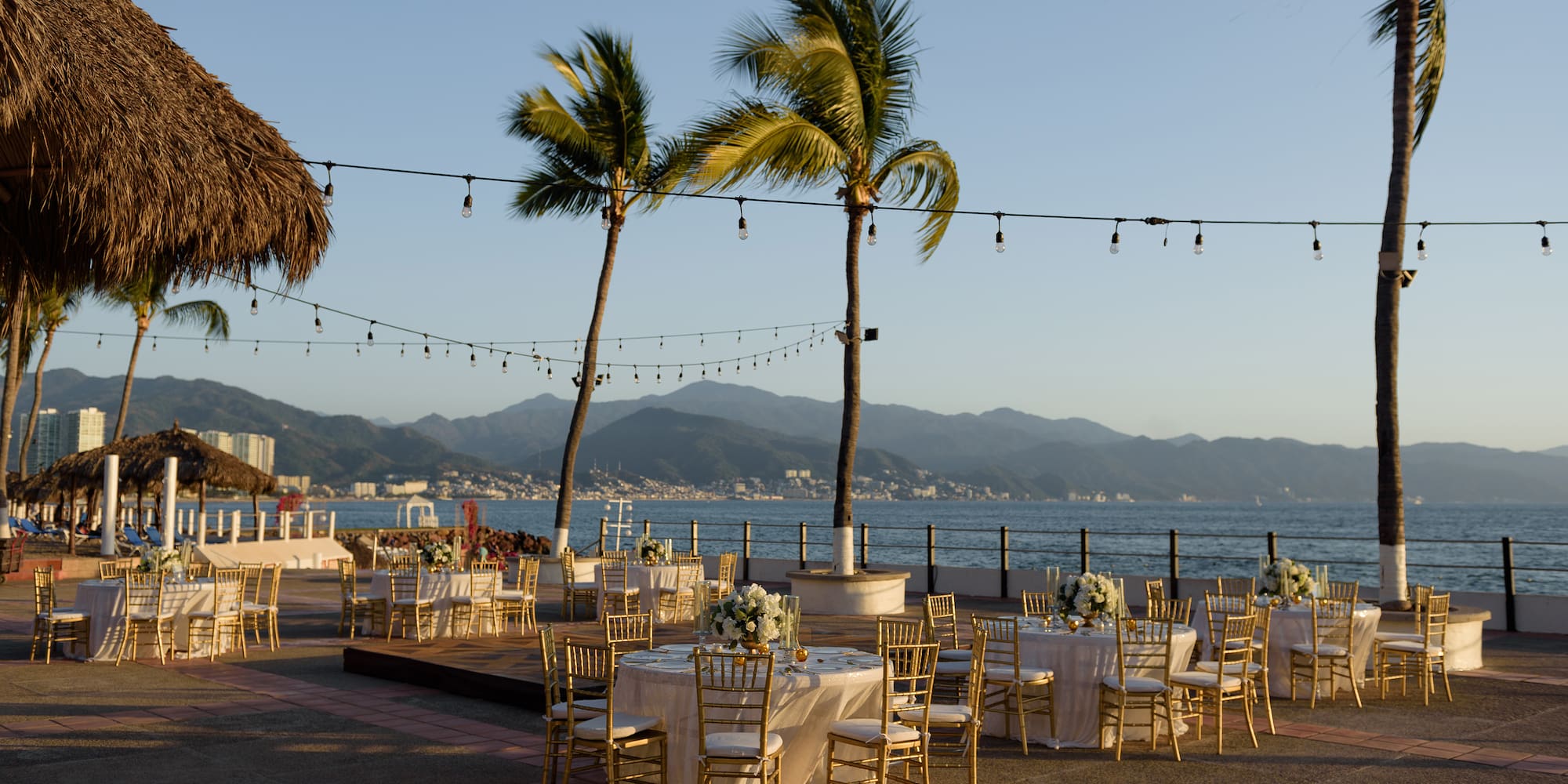 a group of tables and chairs with palm trees and water in the background