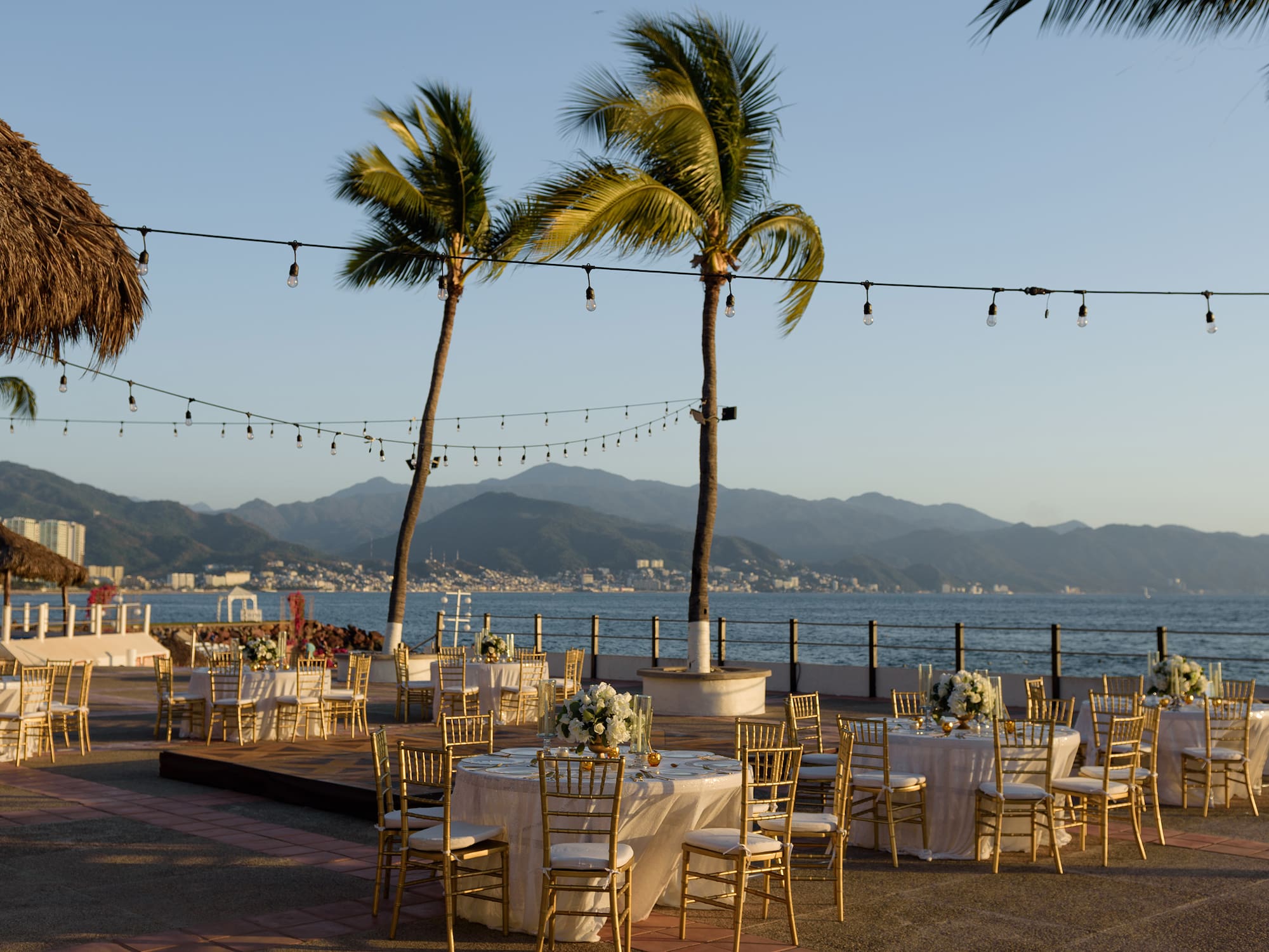 a group of tables and chairs with palm trees and water in the background