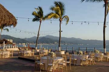 a group of tables and chairs with palm trees and water in the background