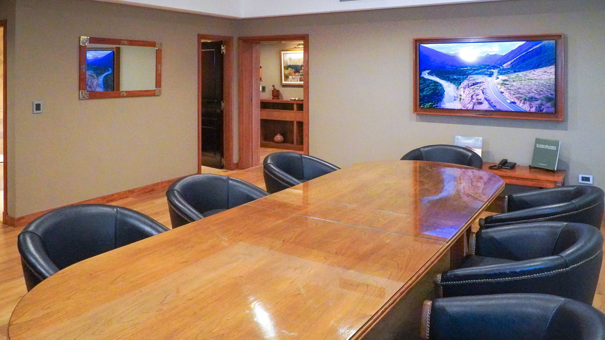 Spacious conference room with long wooden table, black leather chairs, wall TV.