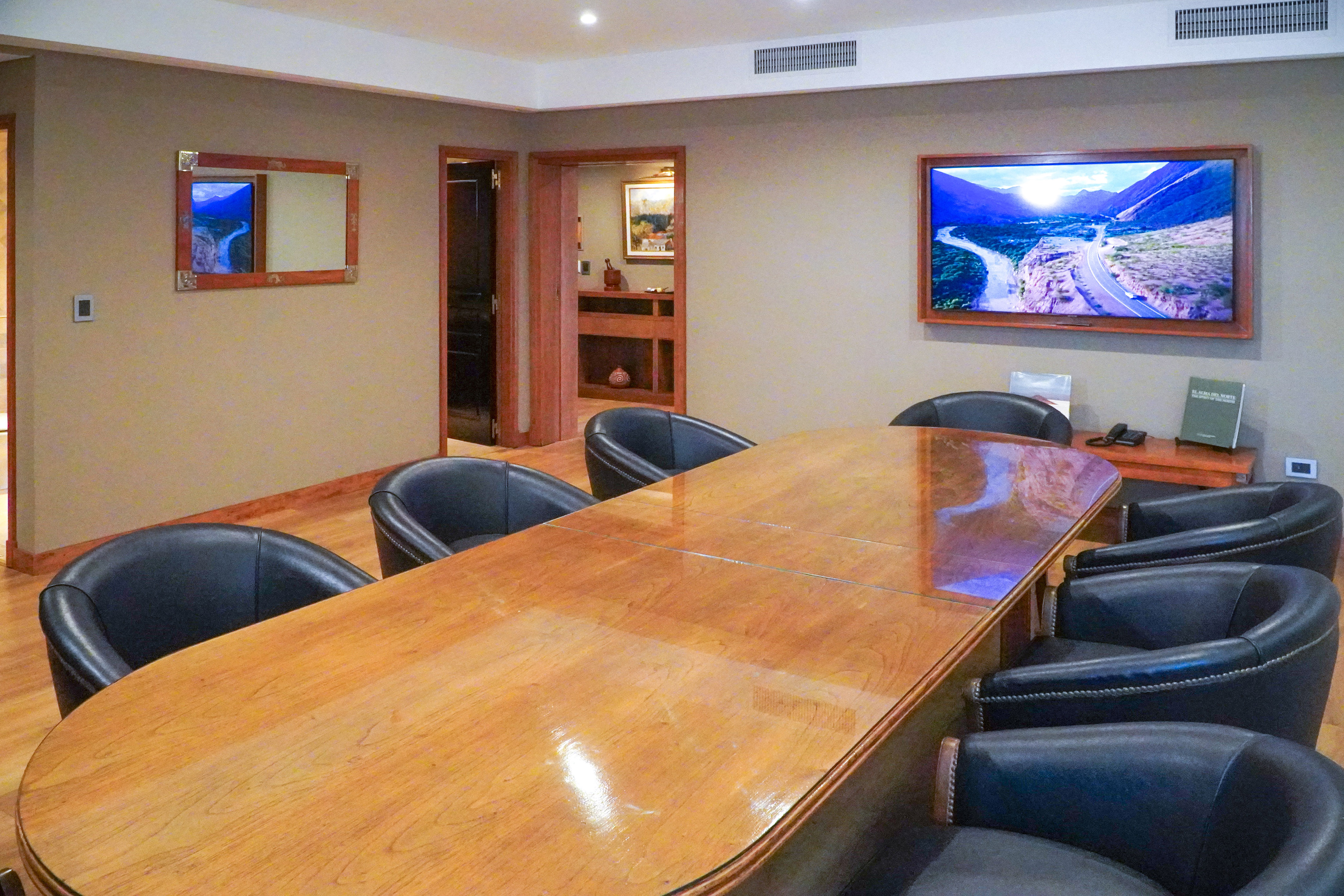 Spacious conference room with long wooden table, black leather chairs, wall TV.