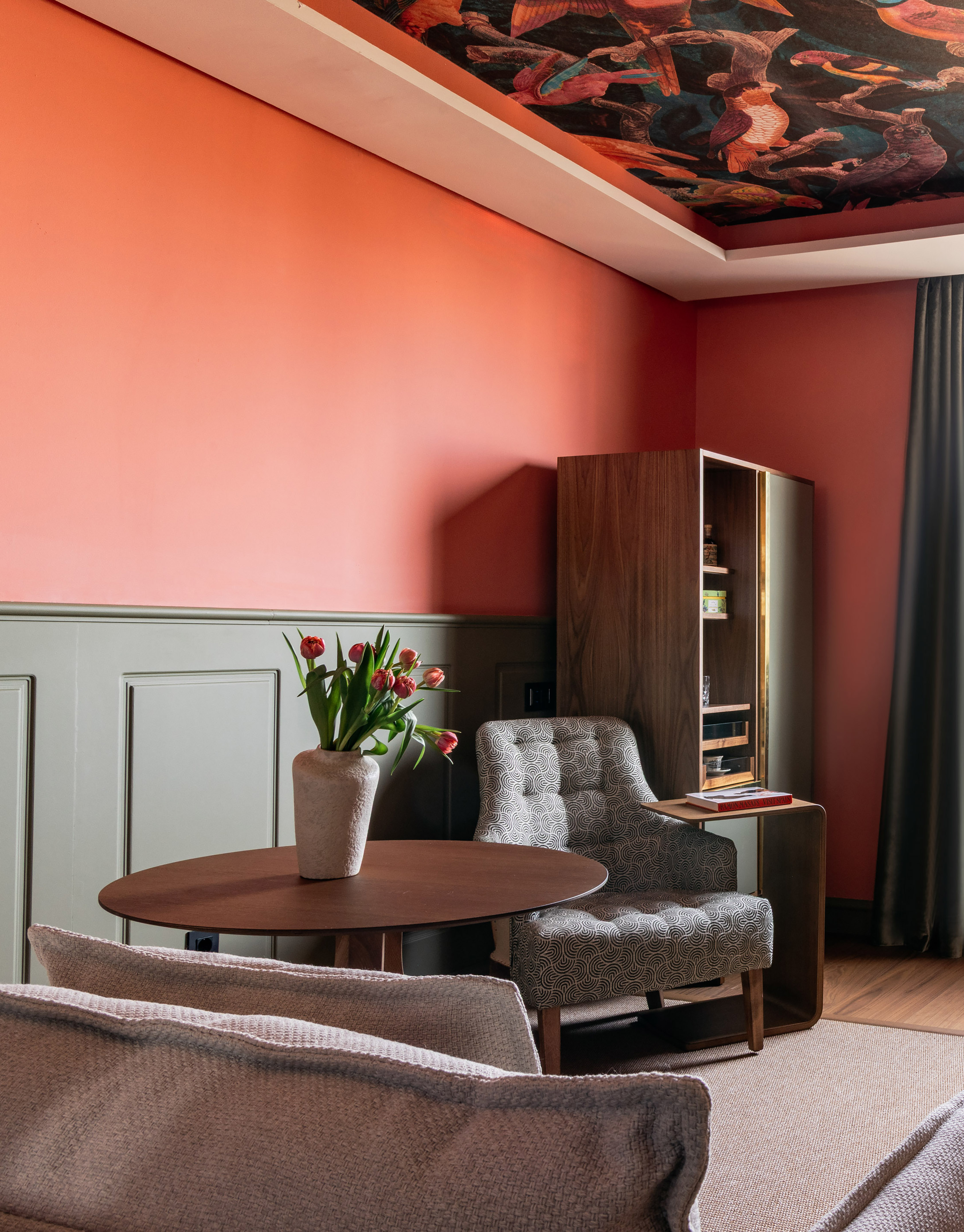 Coral room with bird ceiling wallpaper, tulips, and patterned armchair.
