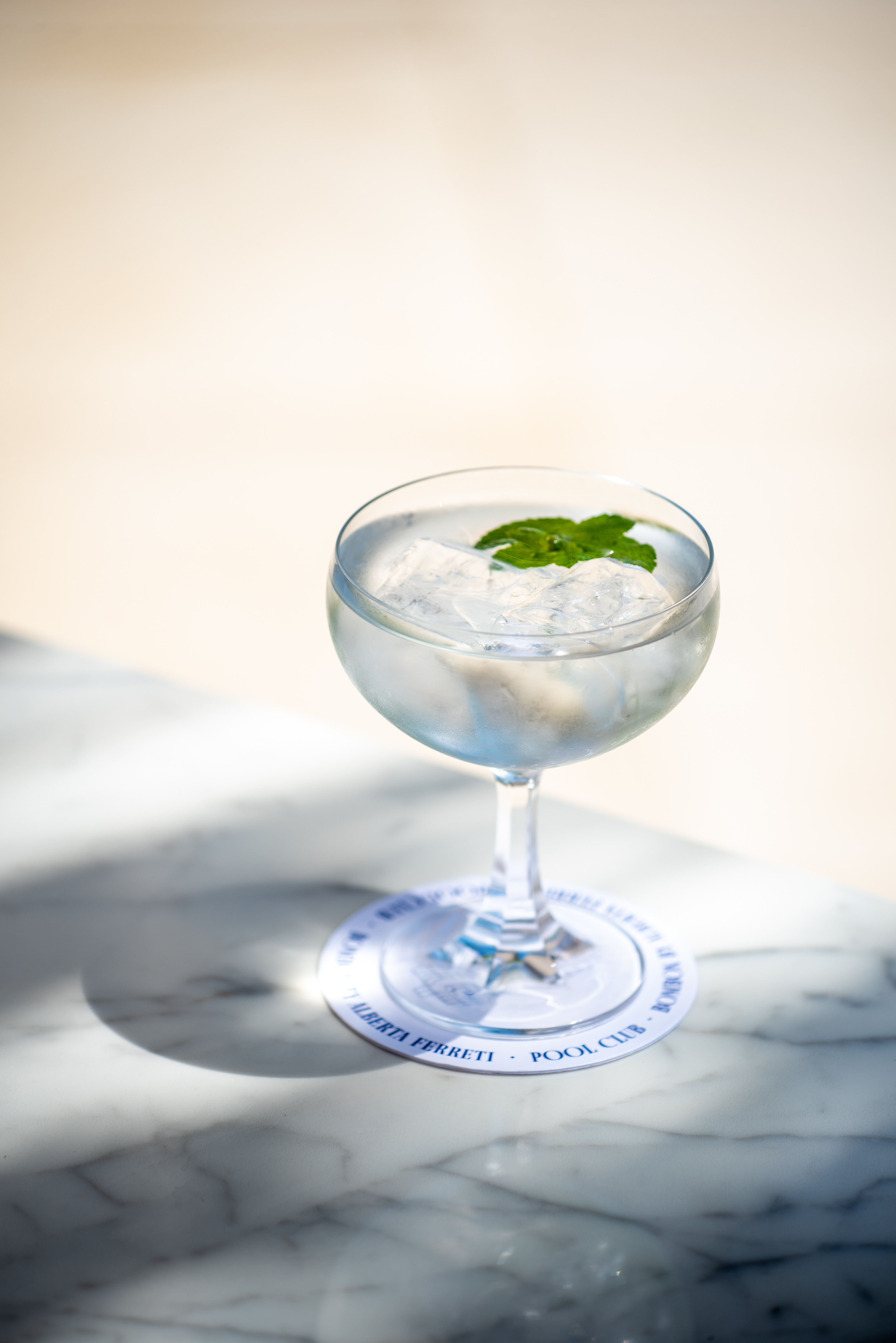 Clear cocktail with mint, ice on Alberta Ferretti Pool Club coaster.