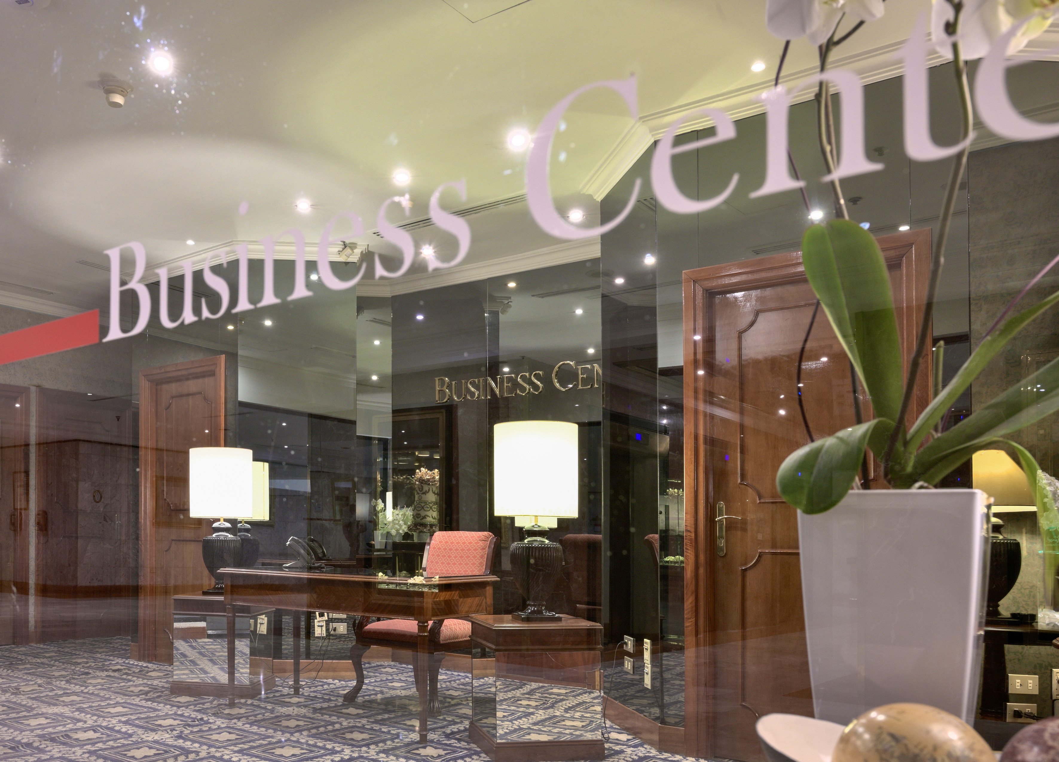Hotel Business Center entrance through glass, with office desk and lamp.