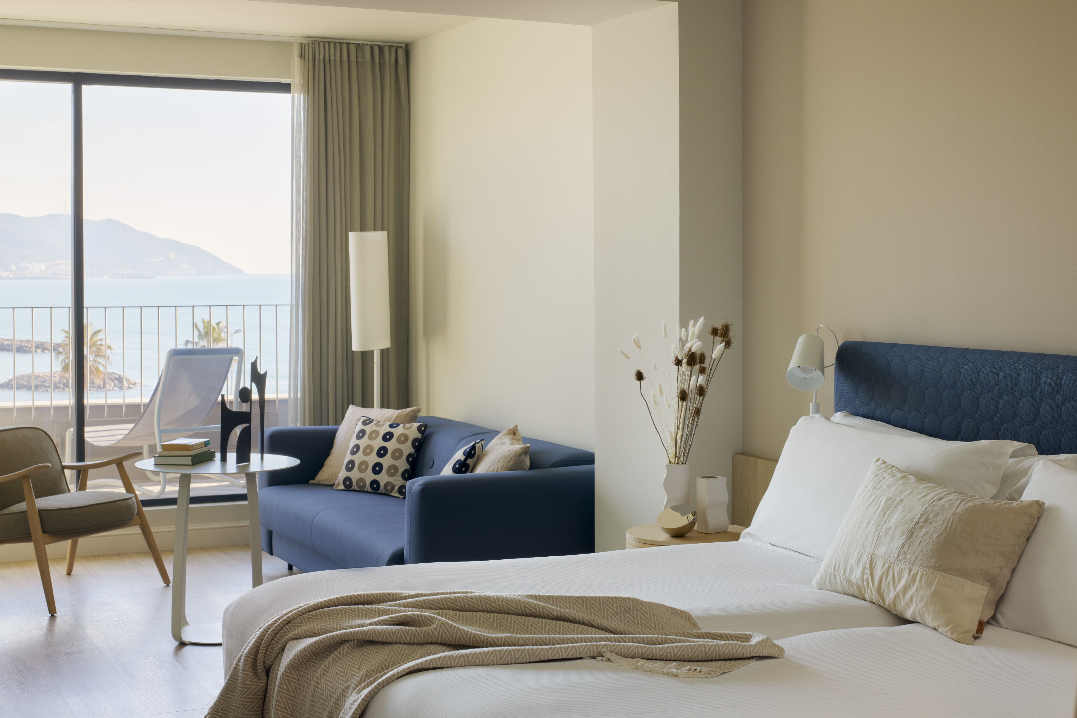 Coastal hotel room with balcony, ocean view, blue sofa, and comfortable bed.