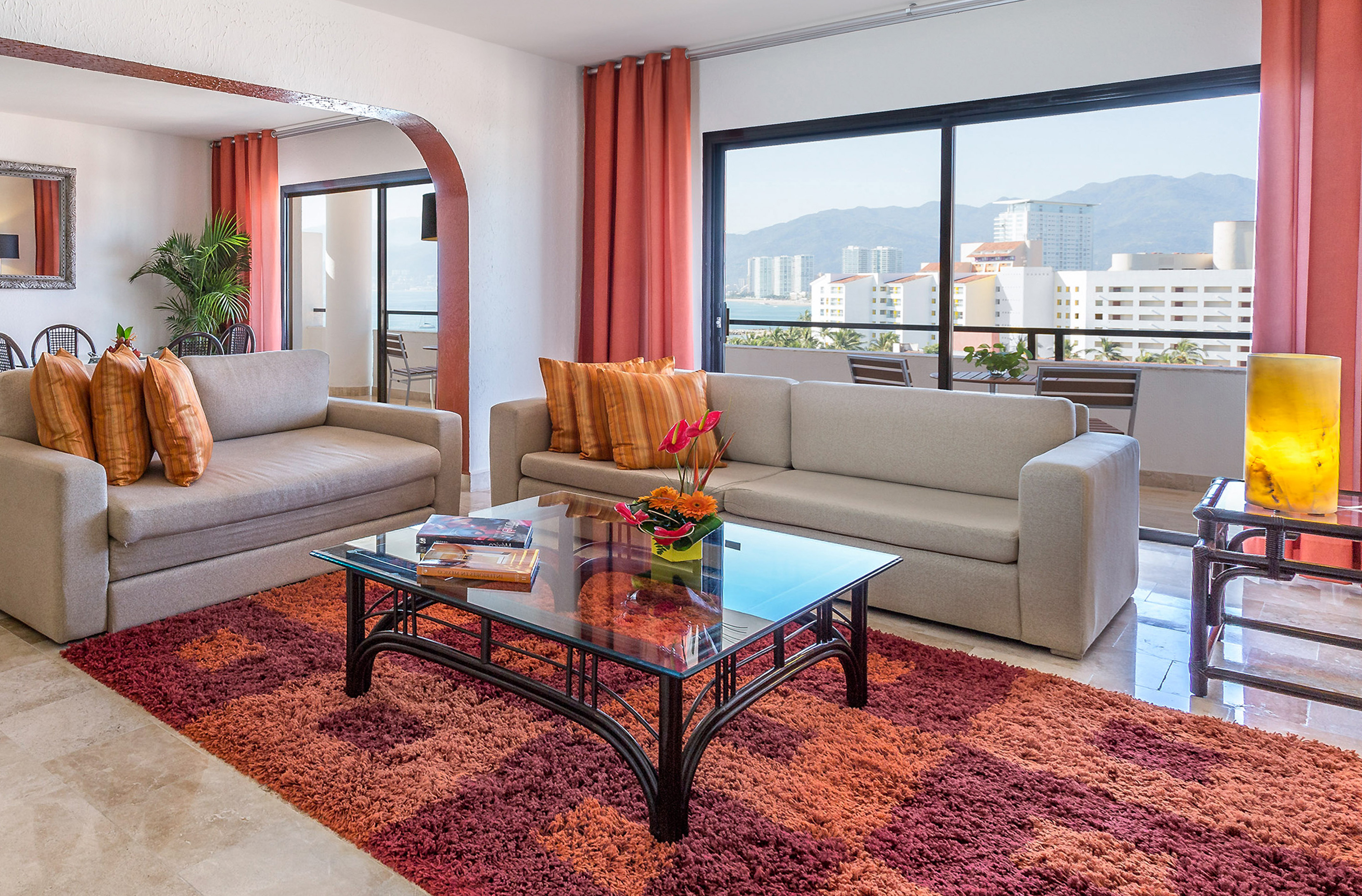 Modern living room with colorful rug, sofas, and panoramic ocean city view.