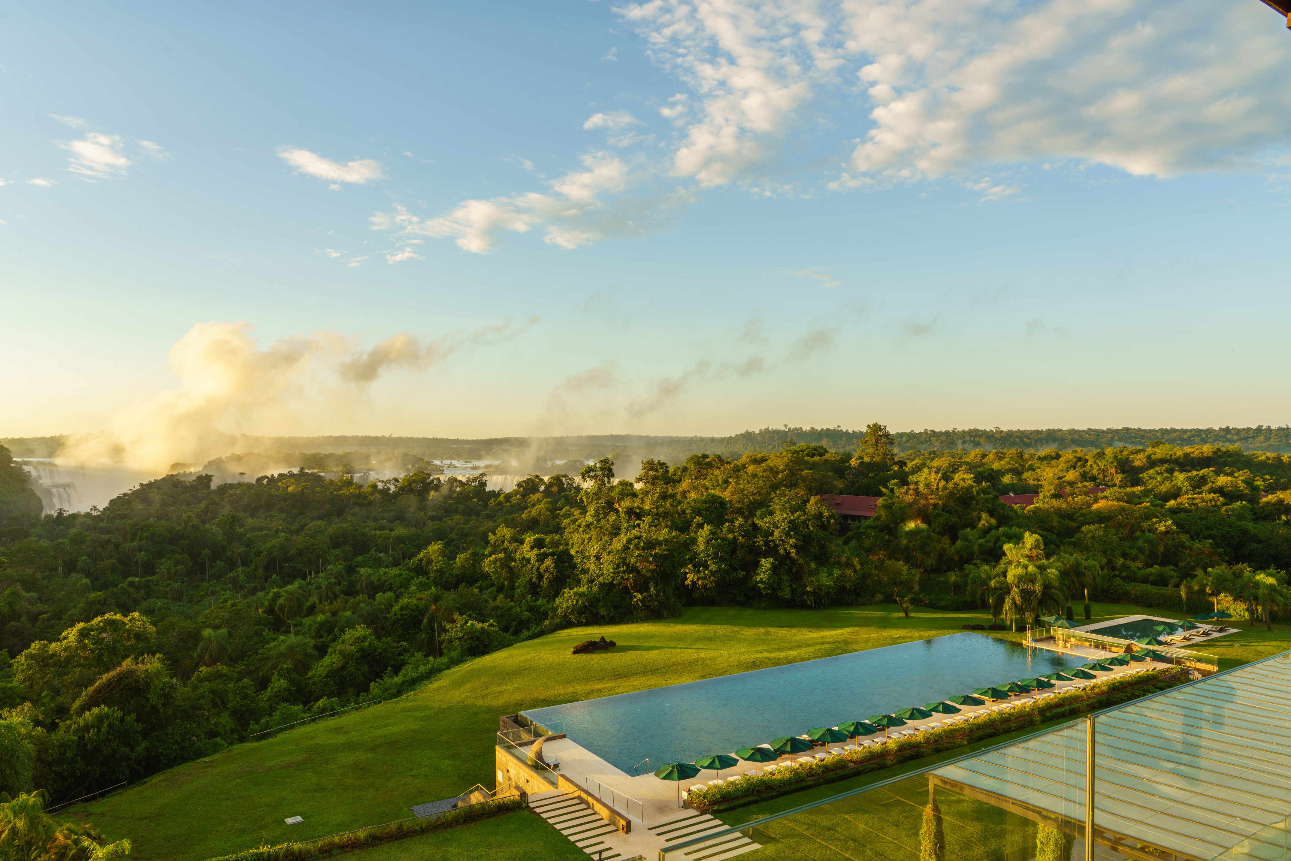 Luxury infinity pool with Iguazu Falls and rainforest, mist rising.