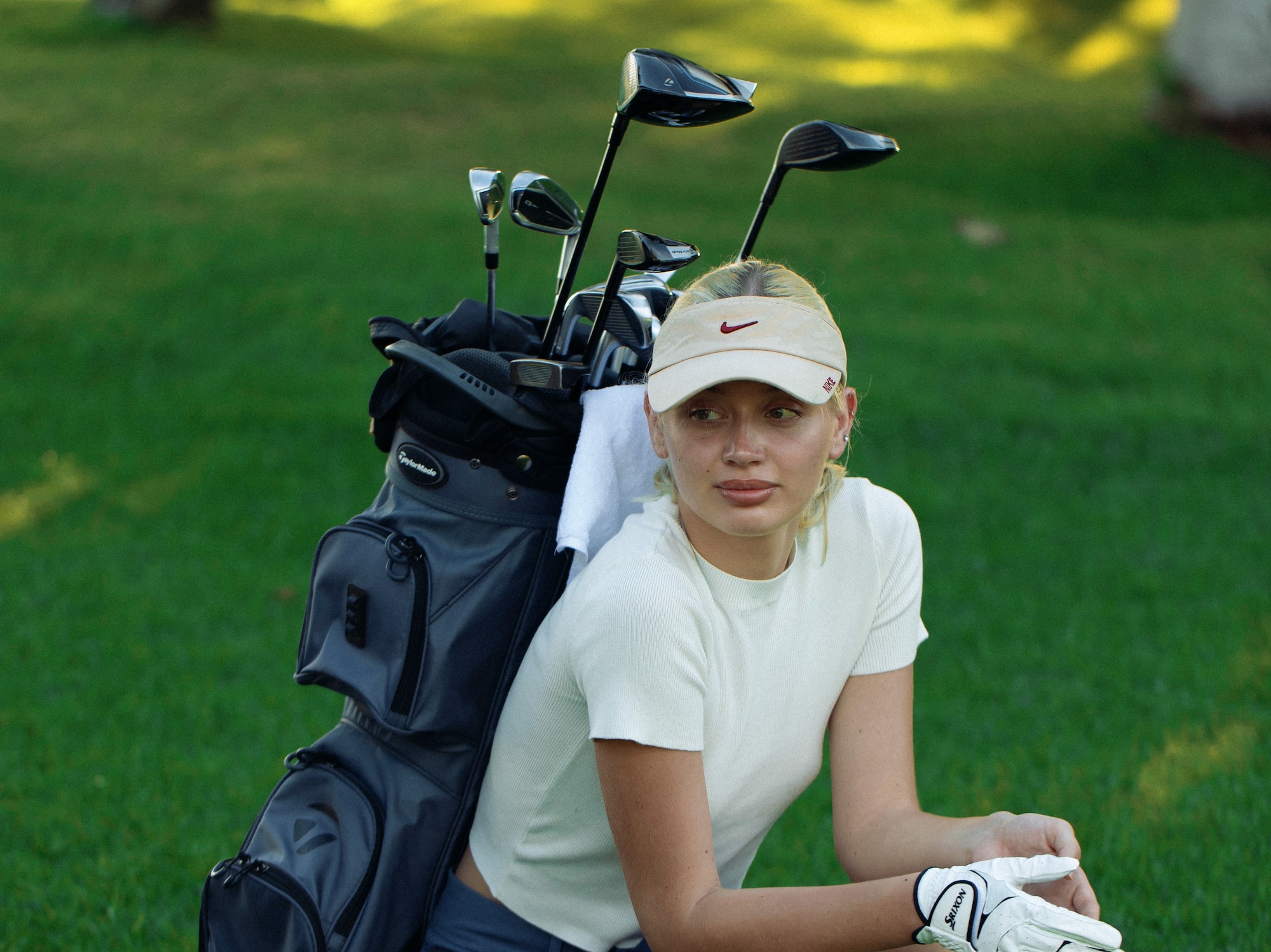 a woman kneeling on grass with golf clubs on back
