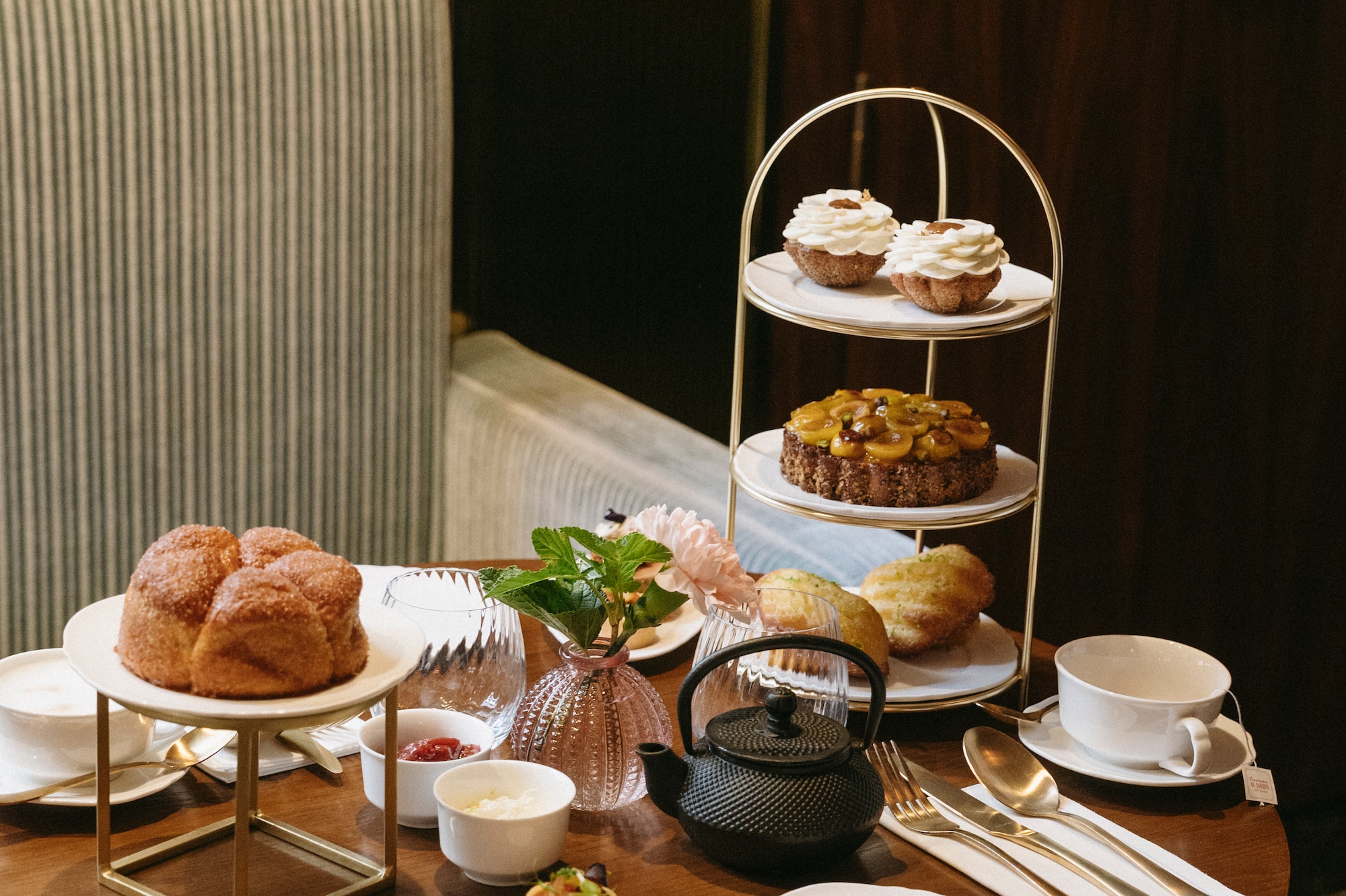 Afternoon tea spread with tiered desserts, brioche, and black teapot on a wooden table.