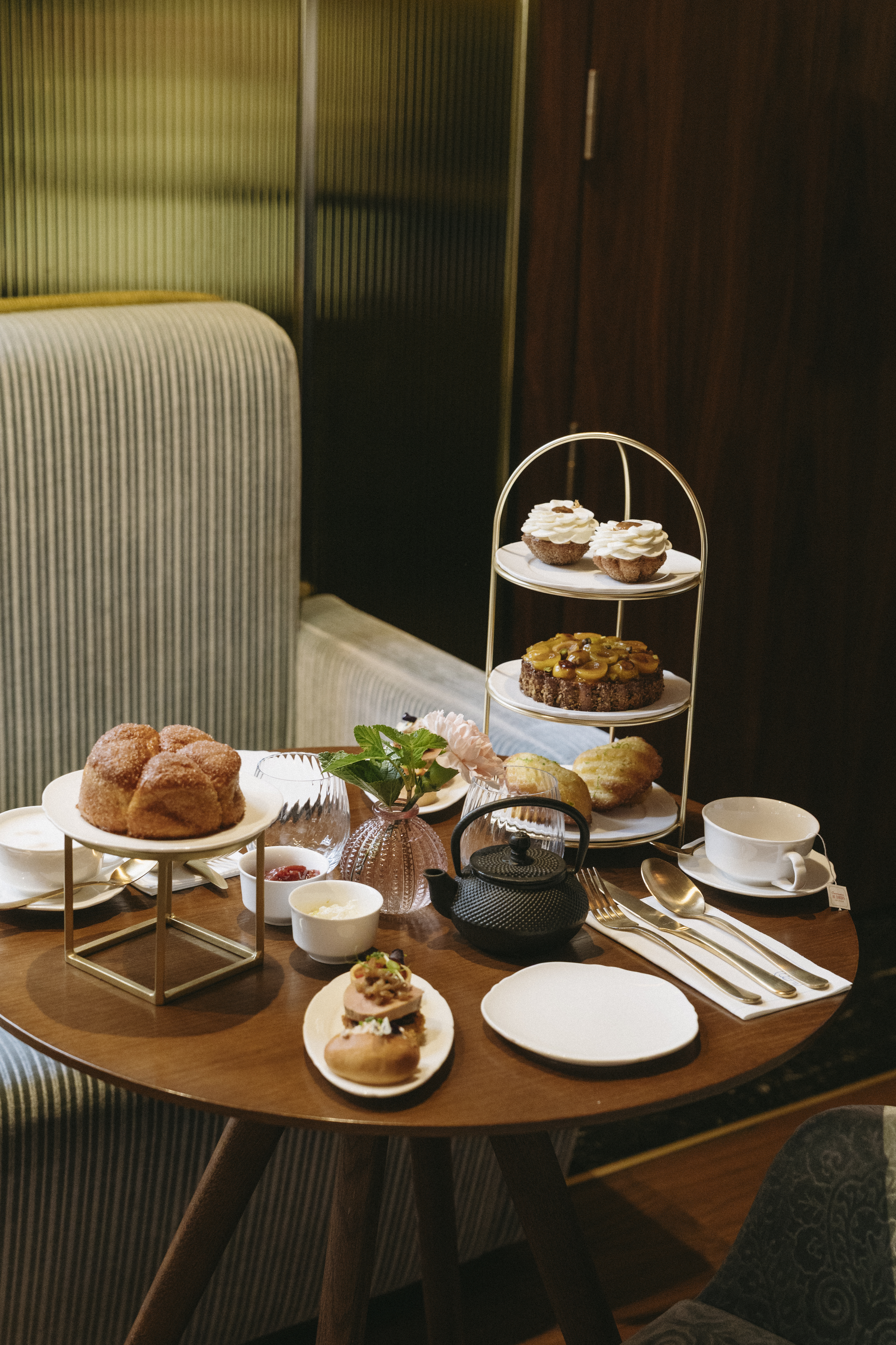 Afternoon tea spread with tiered desserts, brioche, and black teapot on a wooden table.