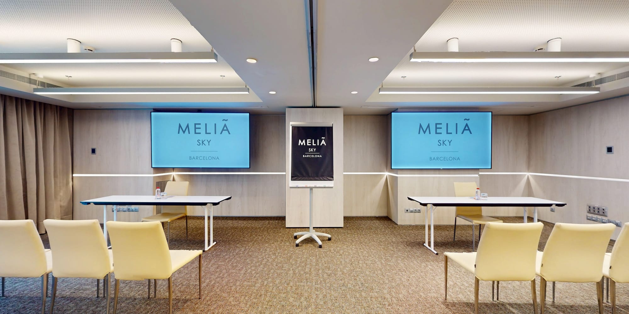 Meliã Sky Barcelona conference room with screens, tables, and beige chairs.