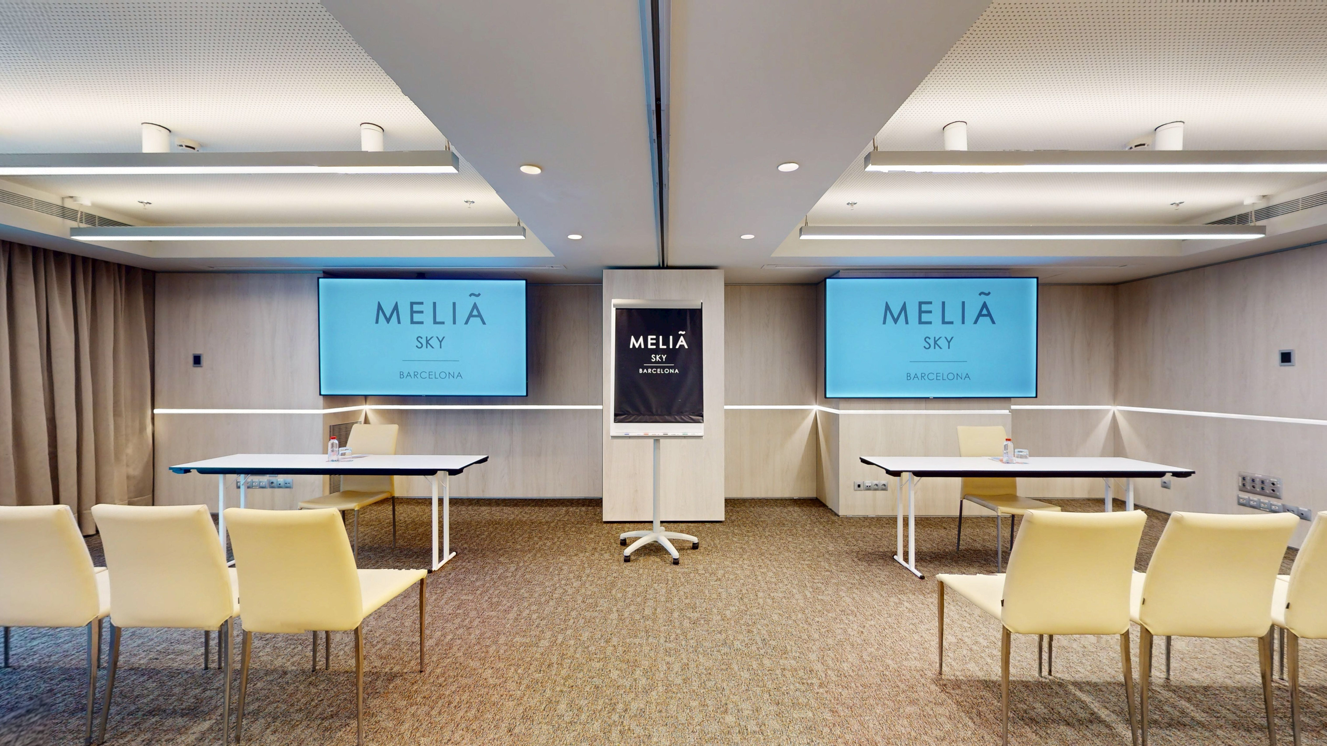 Meliã Sky Barcelona conference room with screens, tables, and beige chairs.