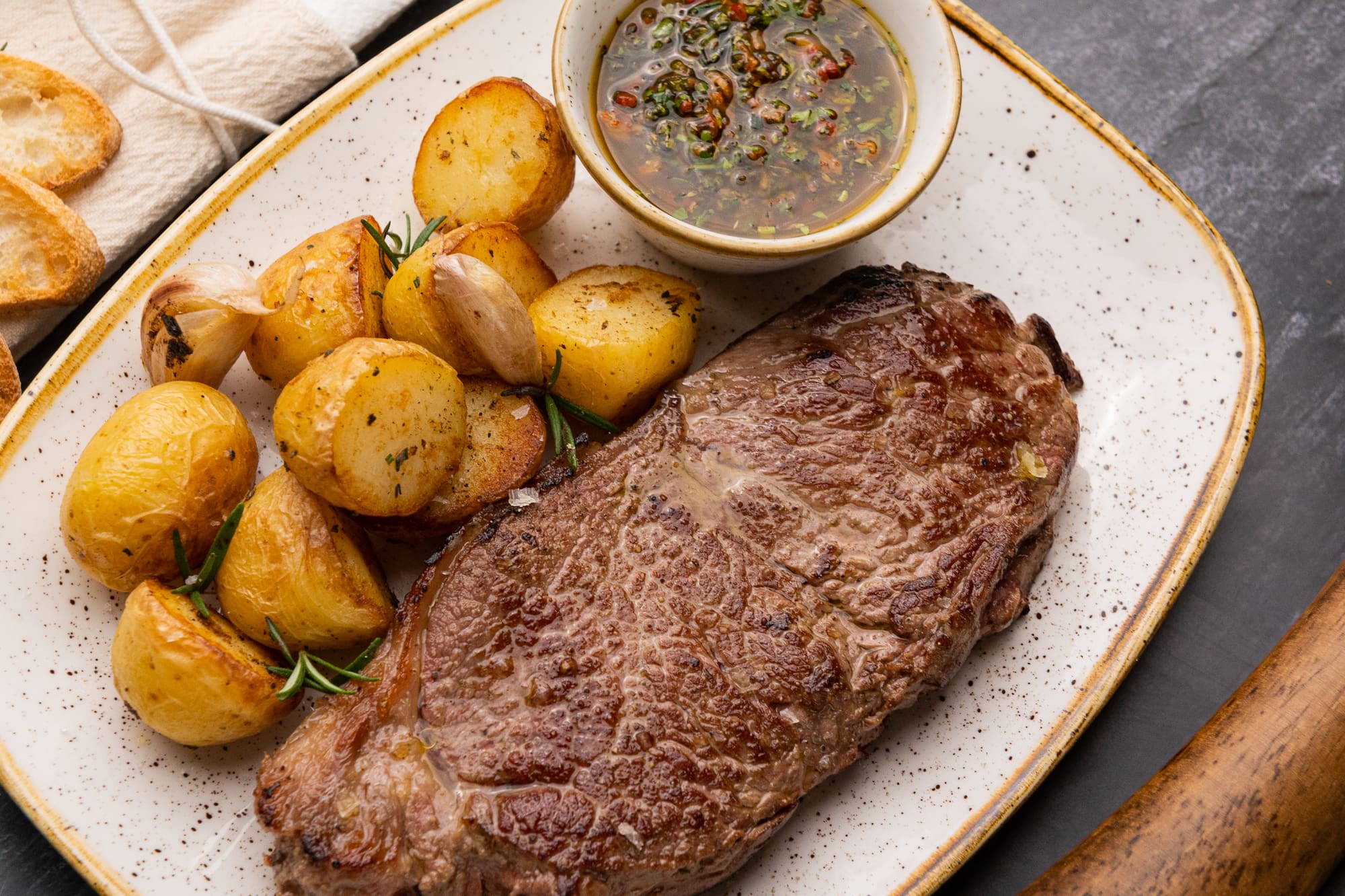 Grilled steak, roasted potatoes with herbs, and a side of chimichurri sauce.