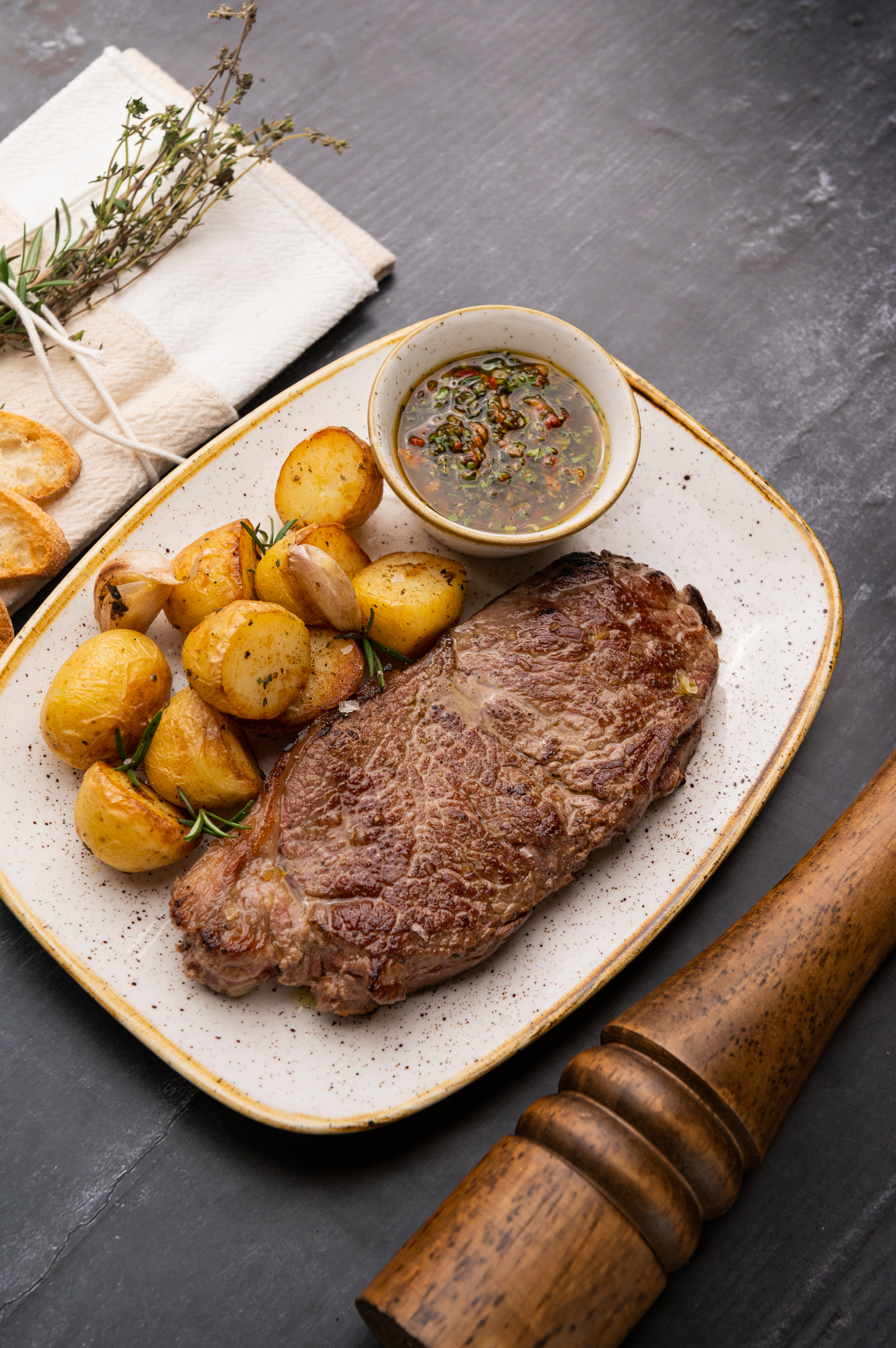 Grilled steak, roasted potatoes with herbs, and a side of chimichurri sauce.