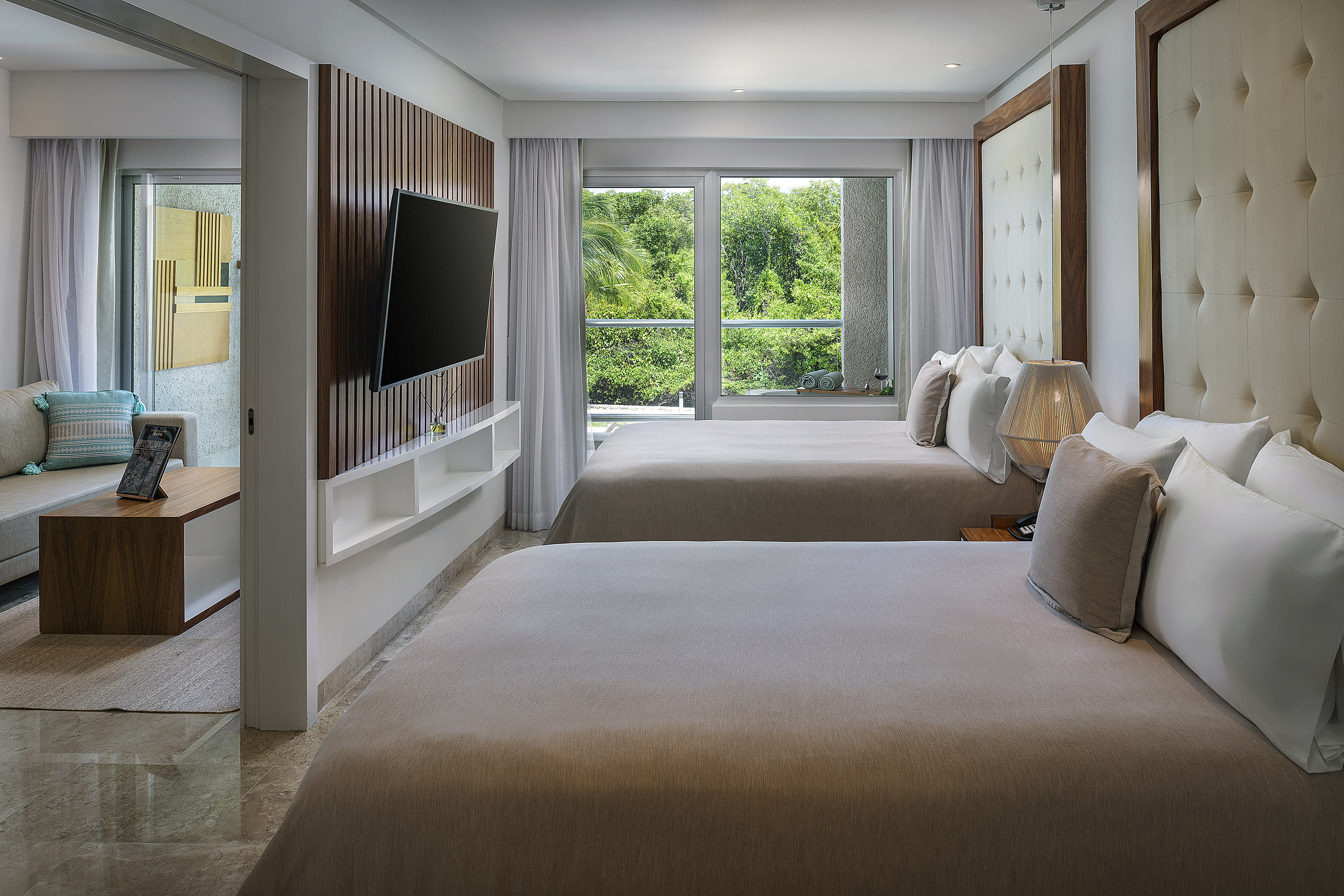 Modern resort room with two beds, tropical view, and adjoining living space.