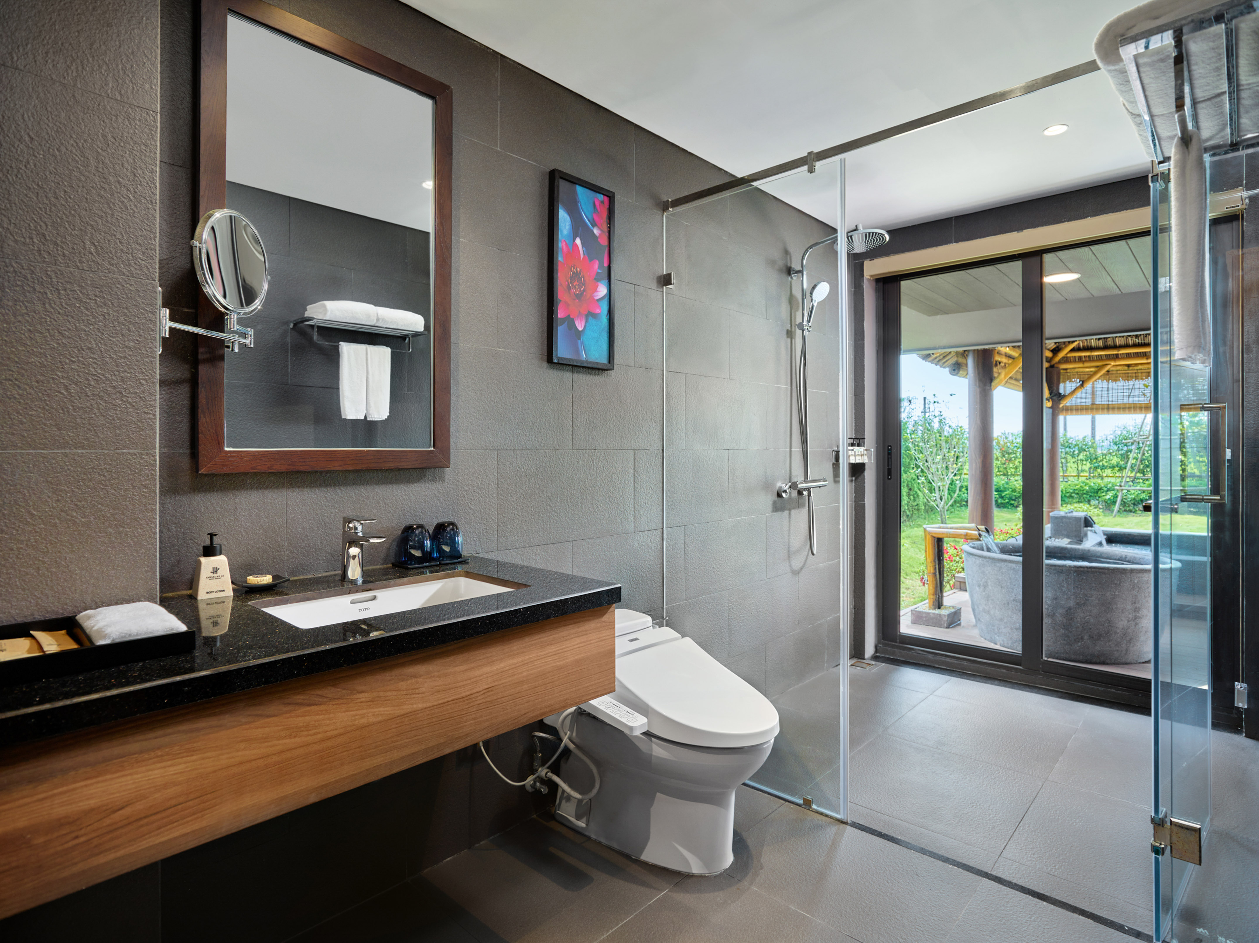 Modern hotel bathroom with gray tiles, wood vanity, shower, toilet, outdoor tub.
