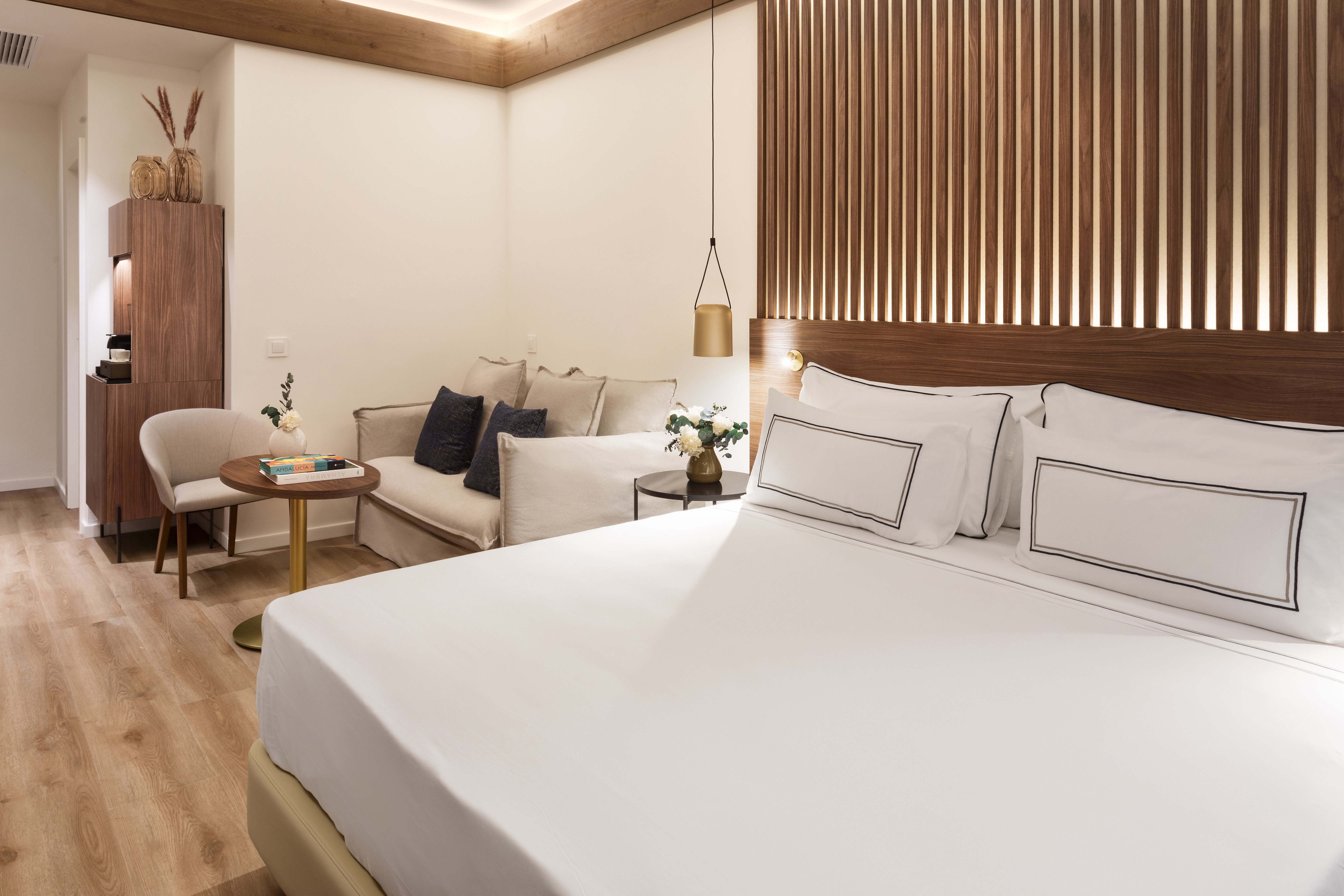 Modern hotel room with bed, wooden headboard, and comfortable lounge area.