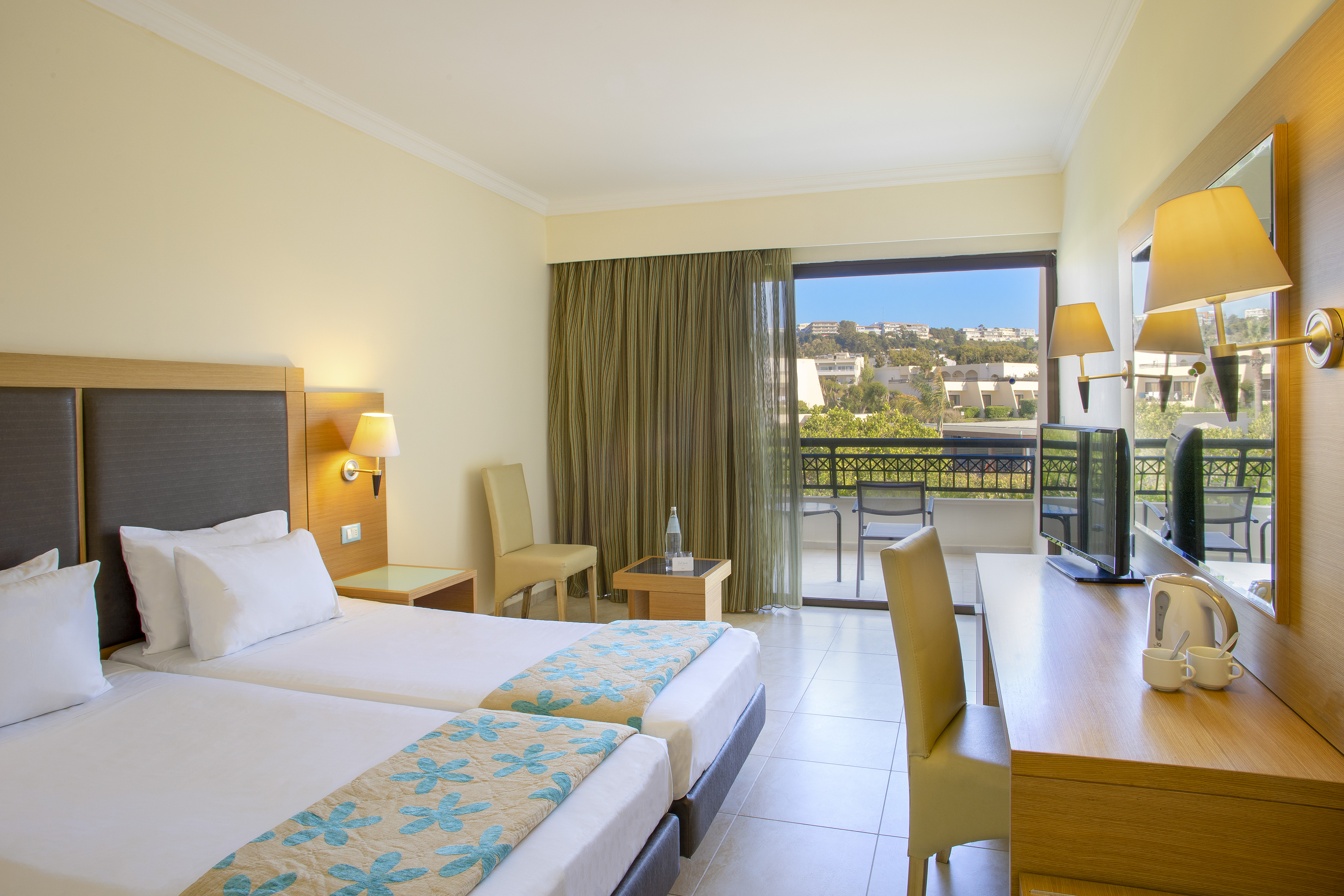 Resort hotel room with twin beds, desk, TV, and balcony view.
