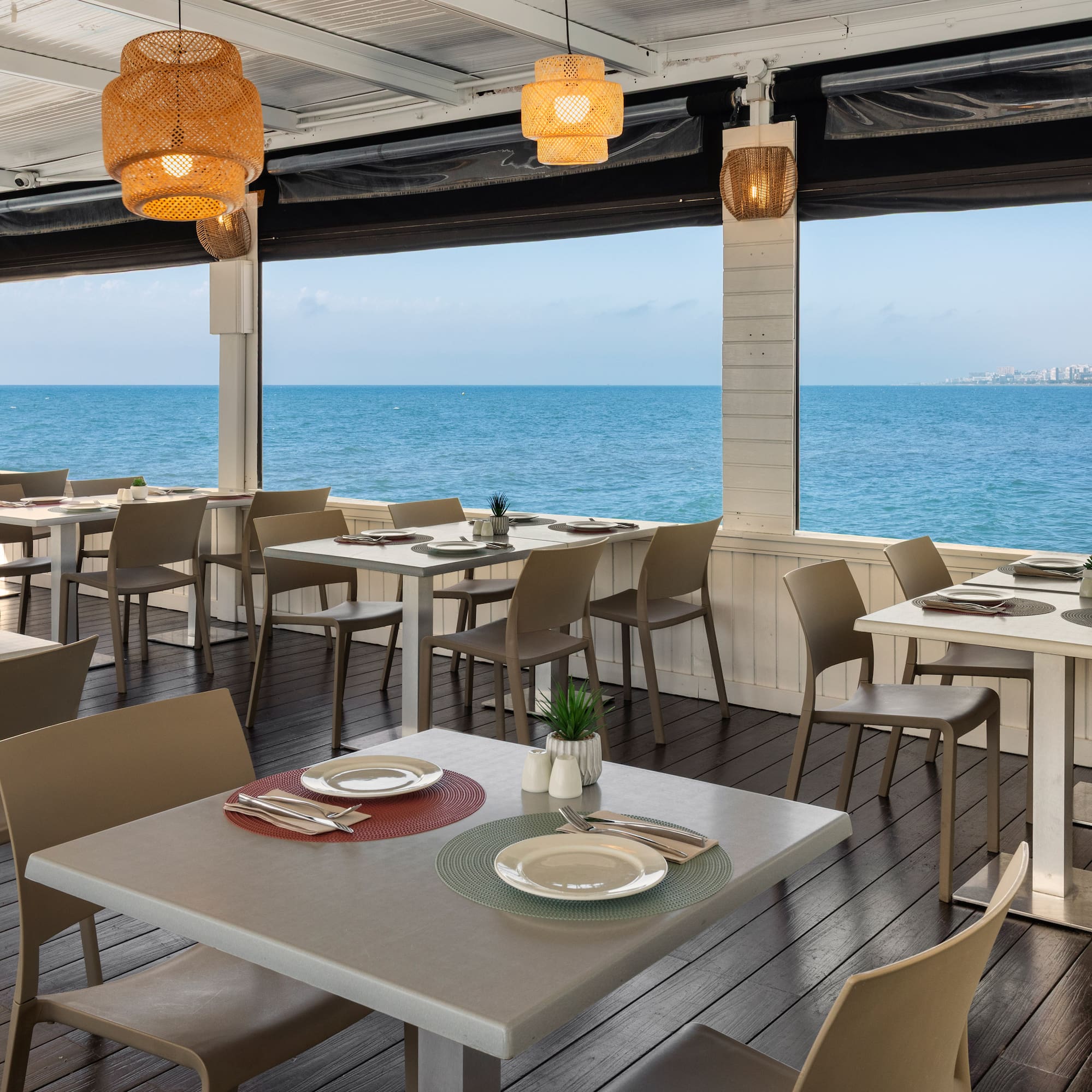 Restaurante costero con terraza, mesas y sillas frente al mar, vista al océano.