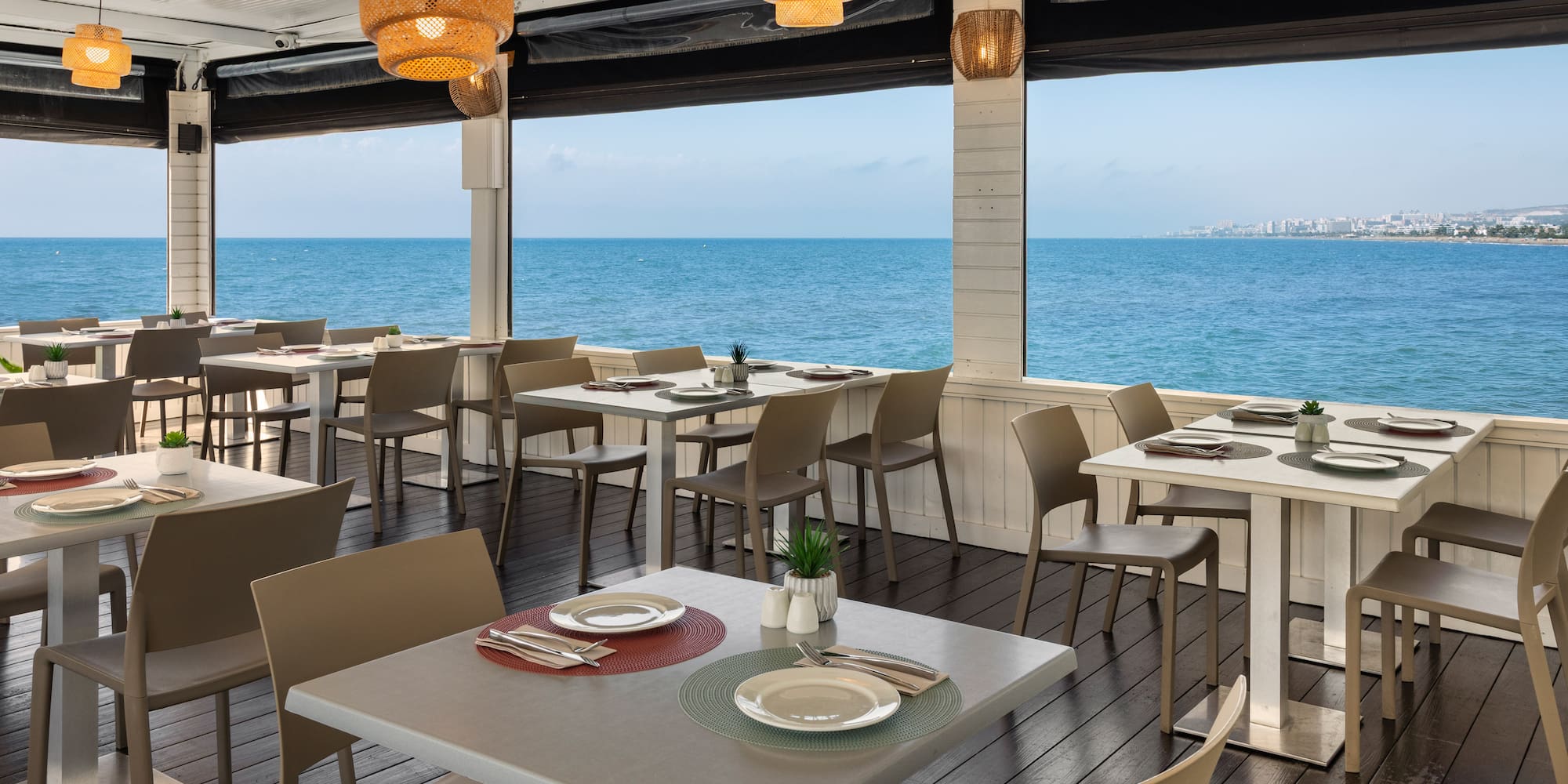 Restaurante terraza frente al mar, mesas puestas, vista panorámica costera.