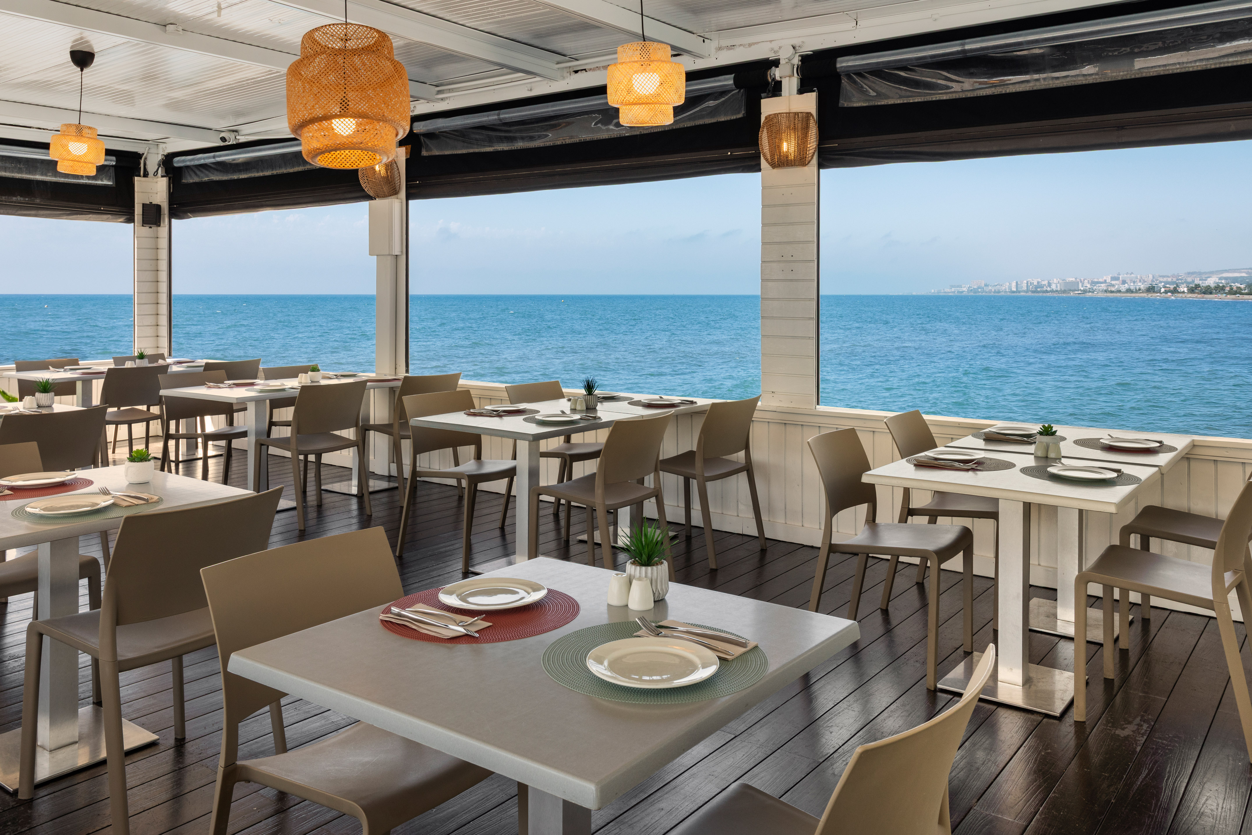 Restaurante terraza frente al mar, mesas puestas, vista panorámica costera.