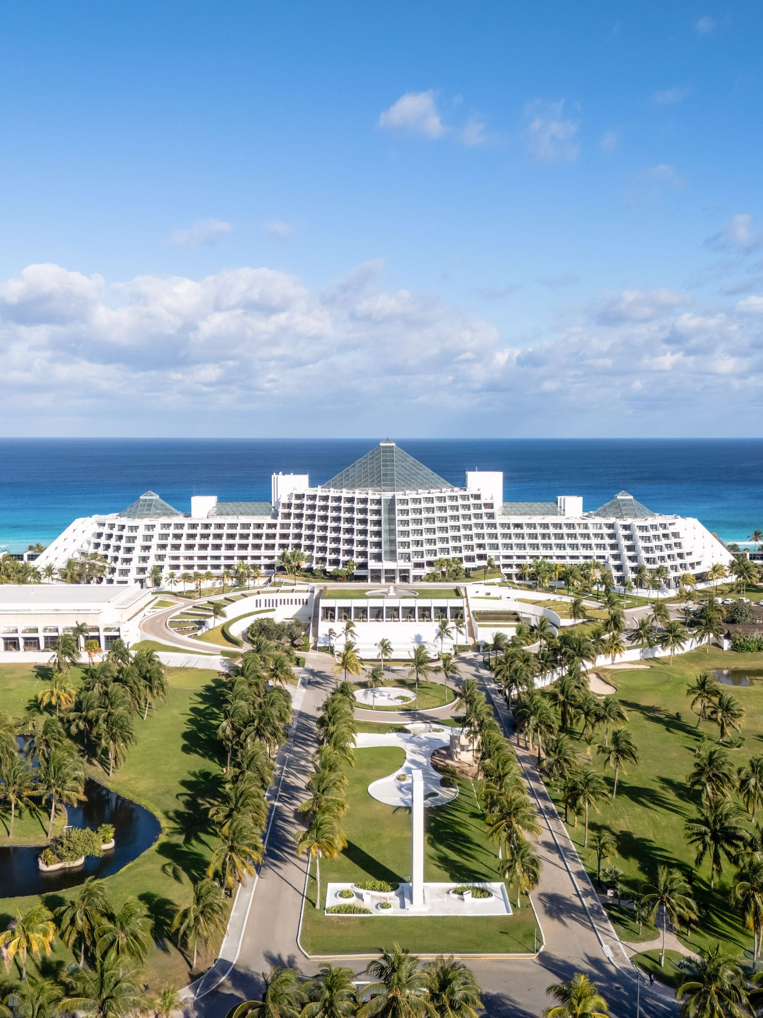 Beach resort with pyramid-shaped buildings, palm-lined drive, and ocean vista.