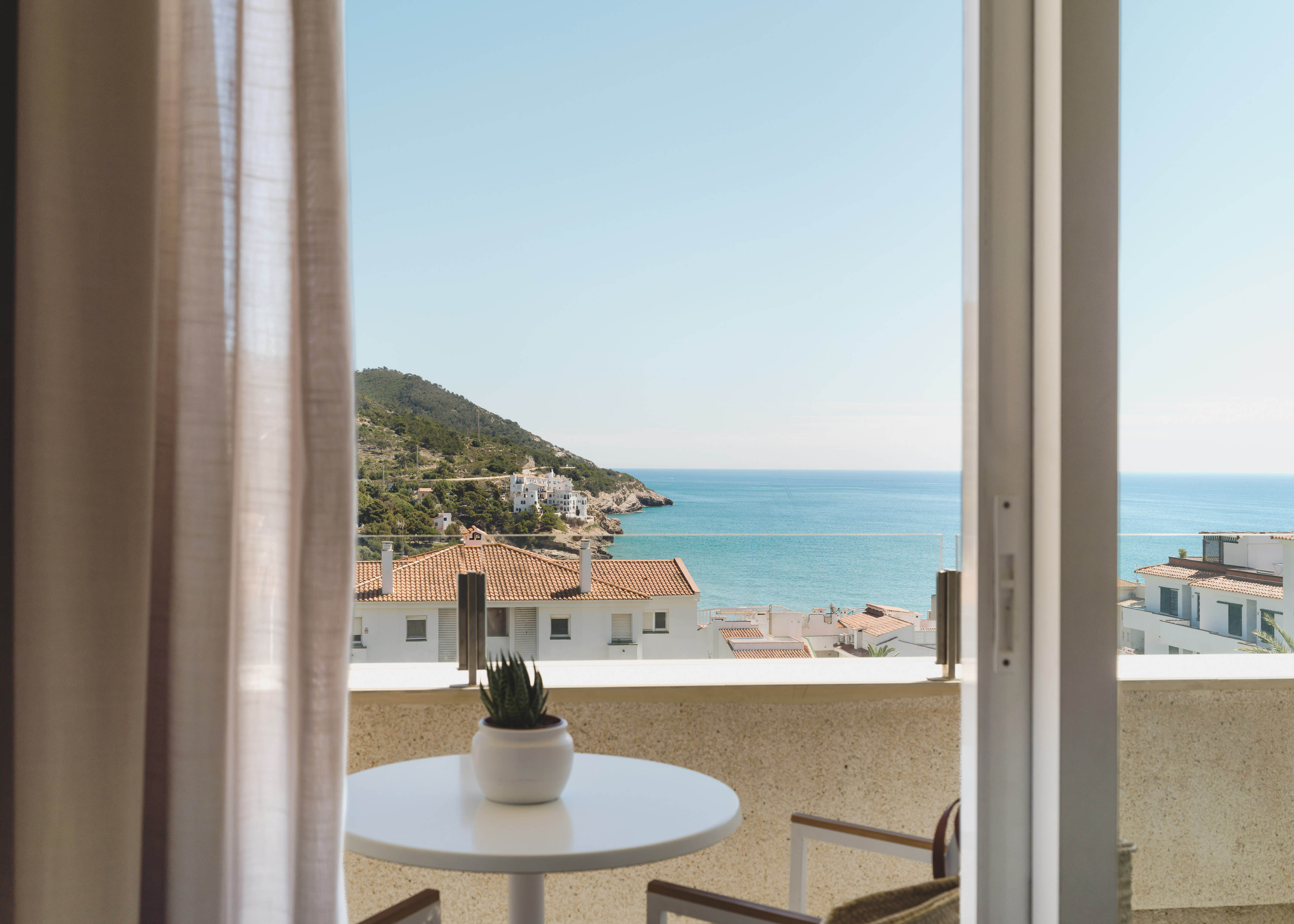 Balcony sea view: coastal village, blue water, green hills under clear sky.