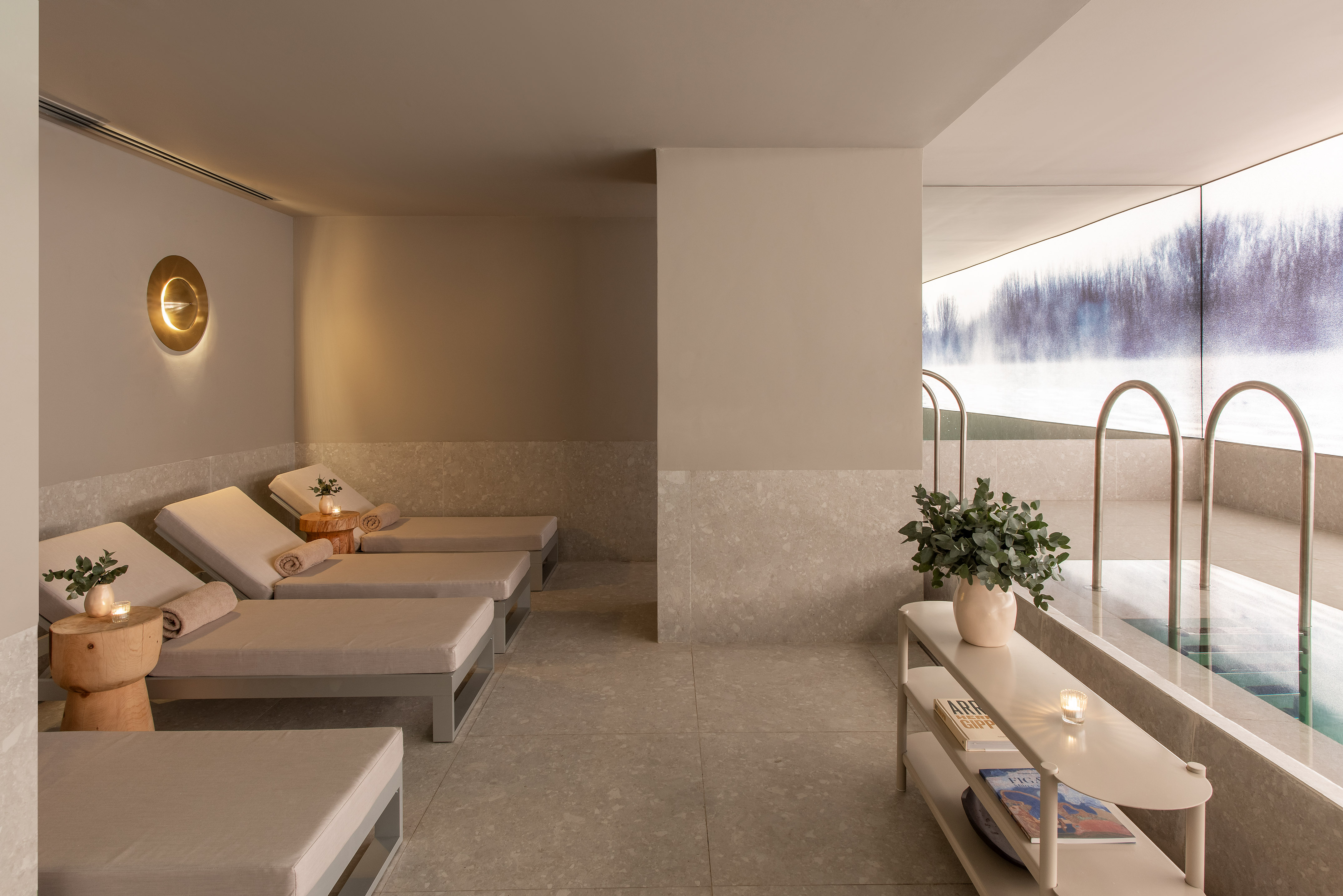 Indoor spa pool and lounge area with modern design and winter forest scene.