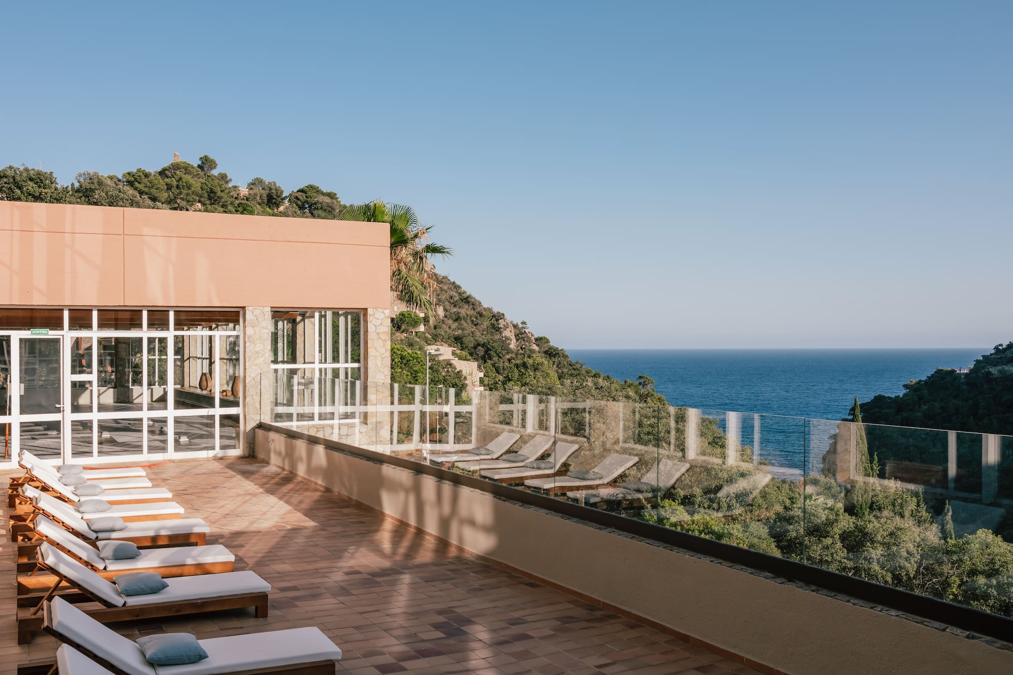 Resort terrace with sun loungers, modern architecture, and scenic ocean view.