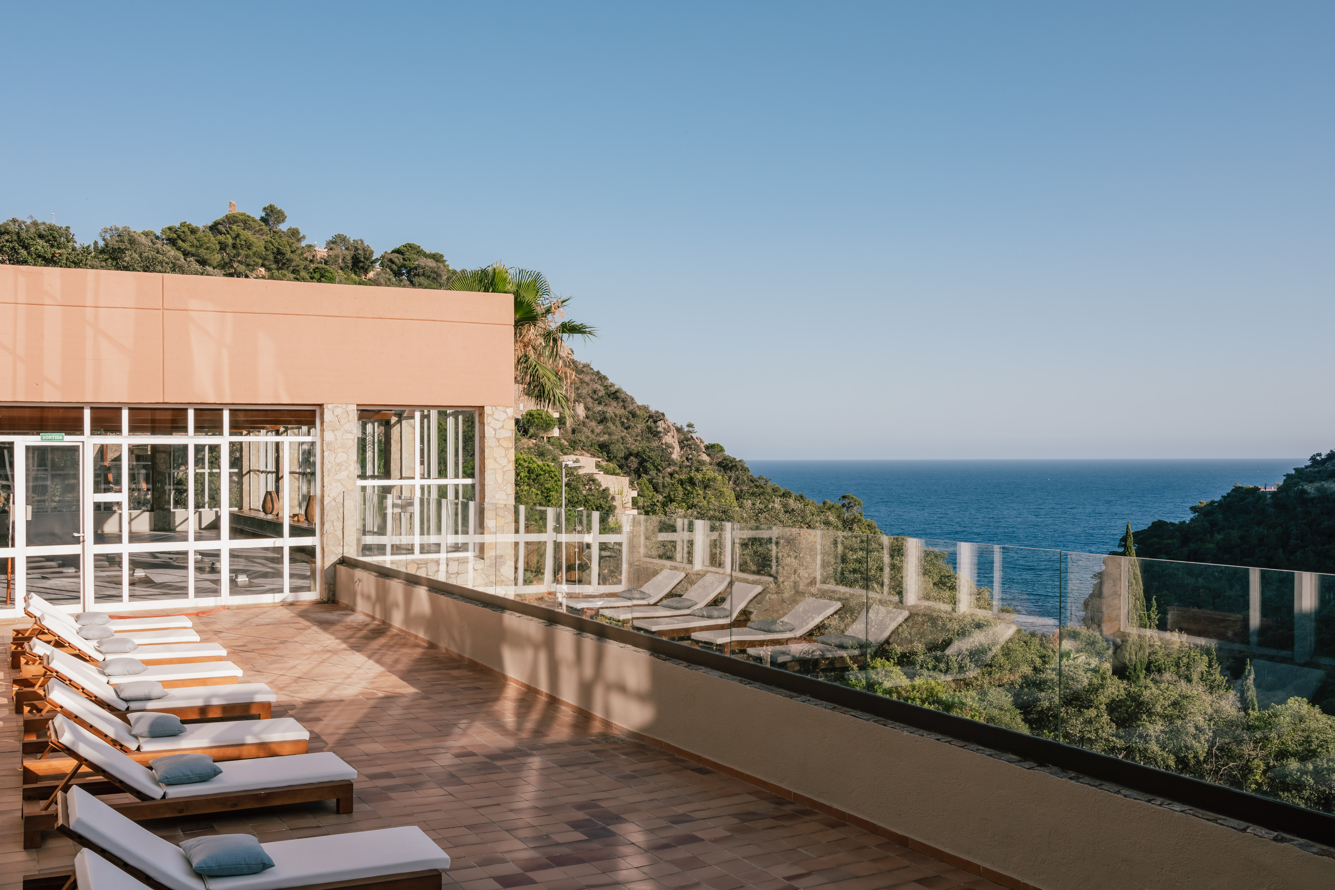 Resort terrace with sun loungers, modern architecture, and scenic ocean view.