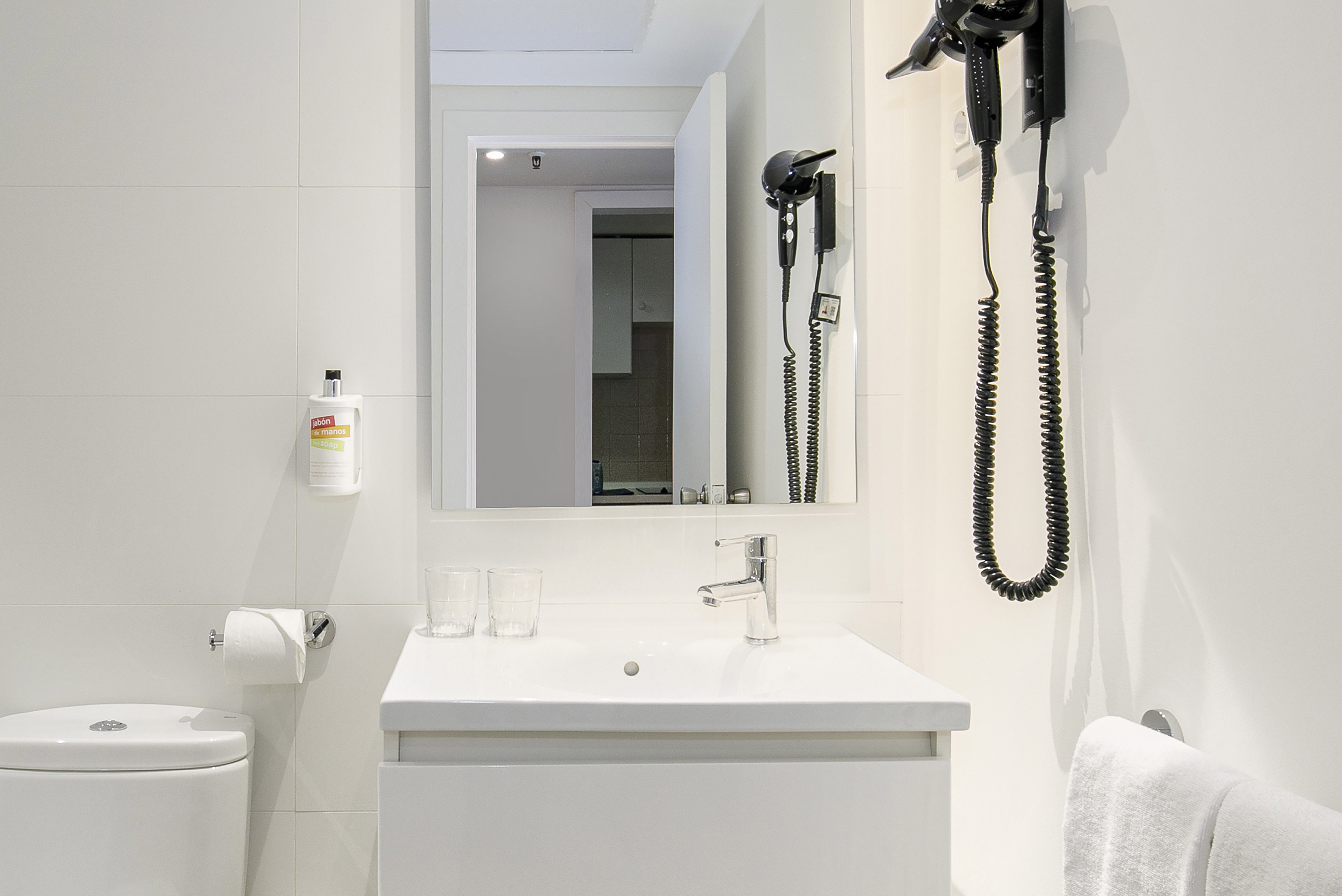 Modern white bathroom with sink, toilet, mirror, hairdryer, and hand soap.