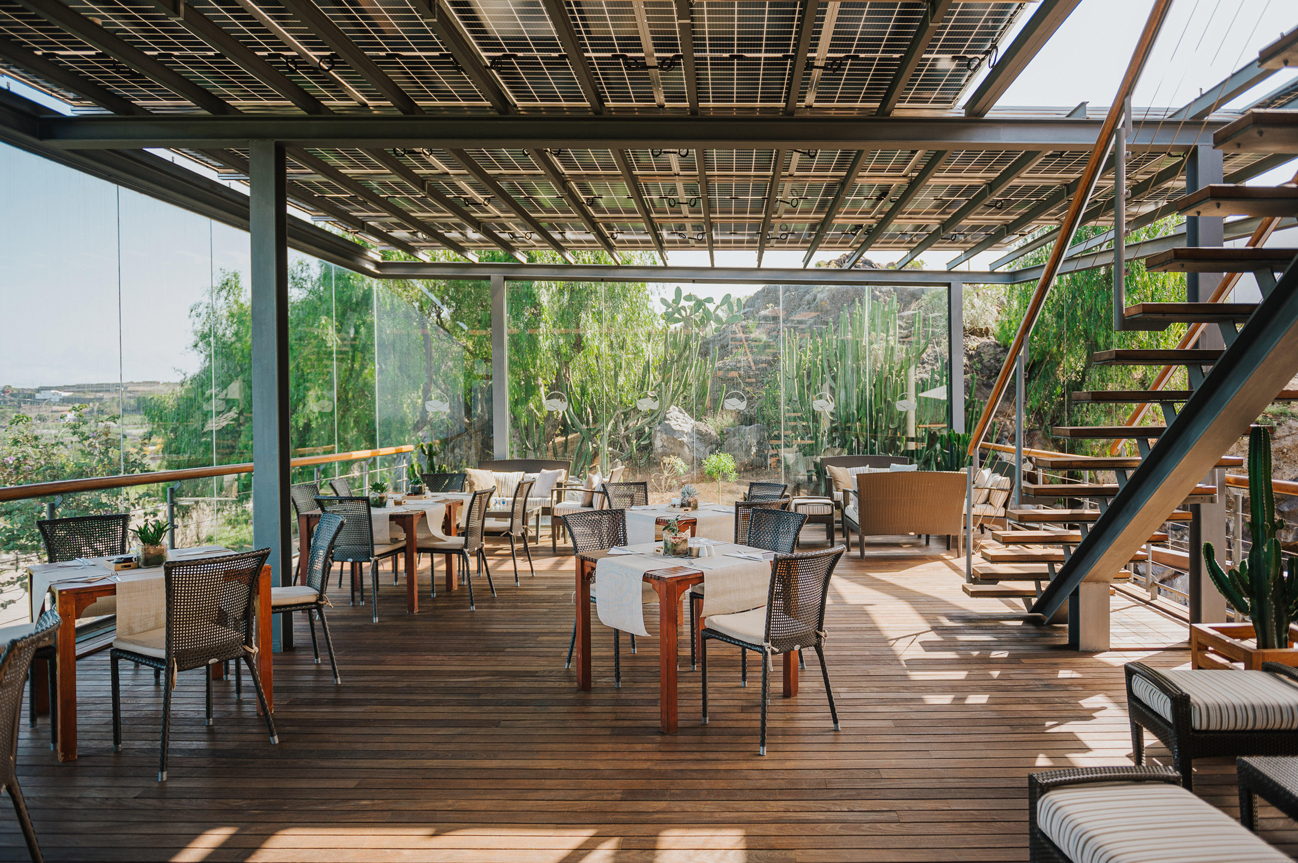 Outdoor restaurant patio under solar roof, with wooden deck and green scenery.