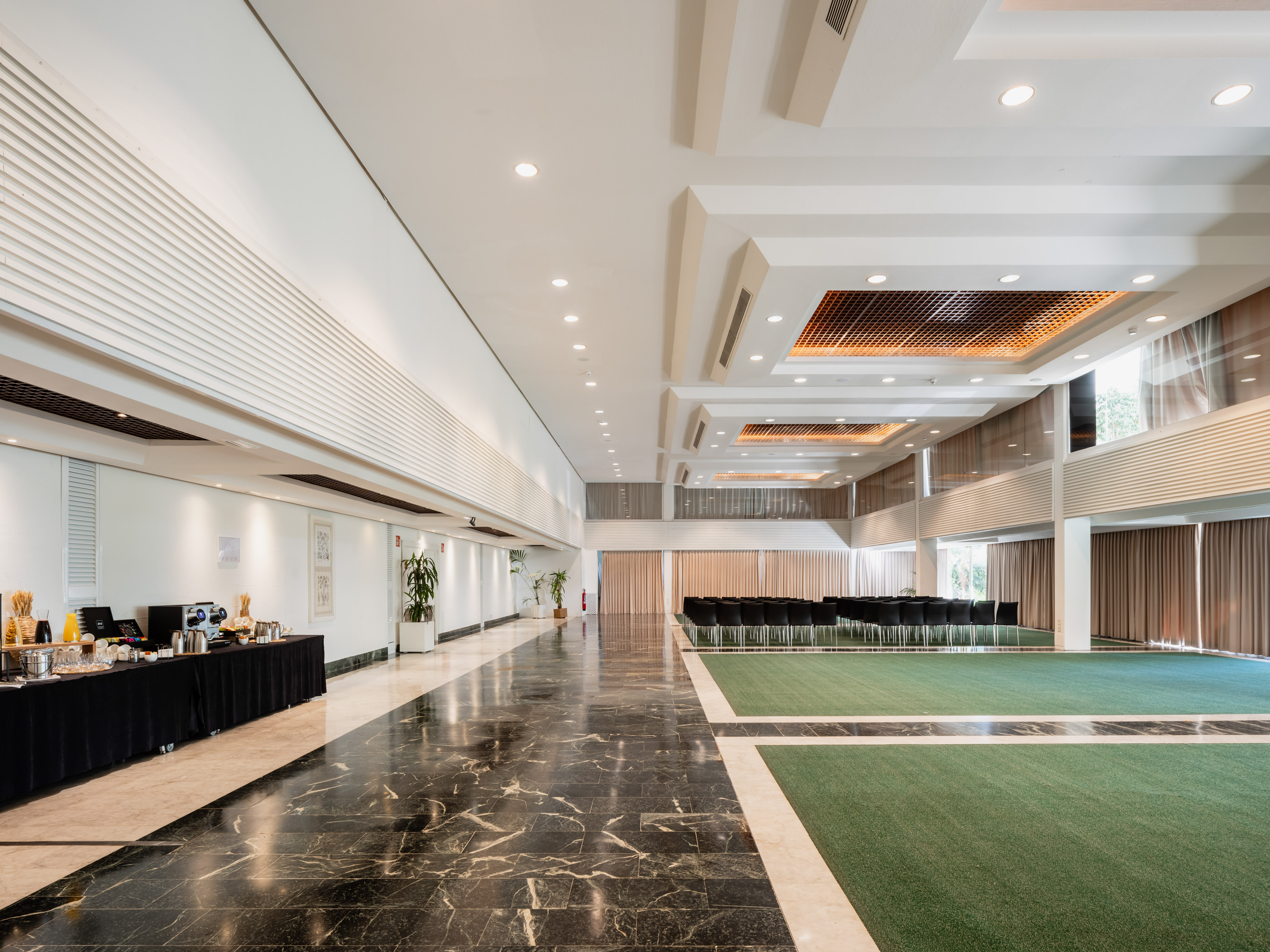 Spacious conference hall with black marble, green carpet, seating, and buffet.