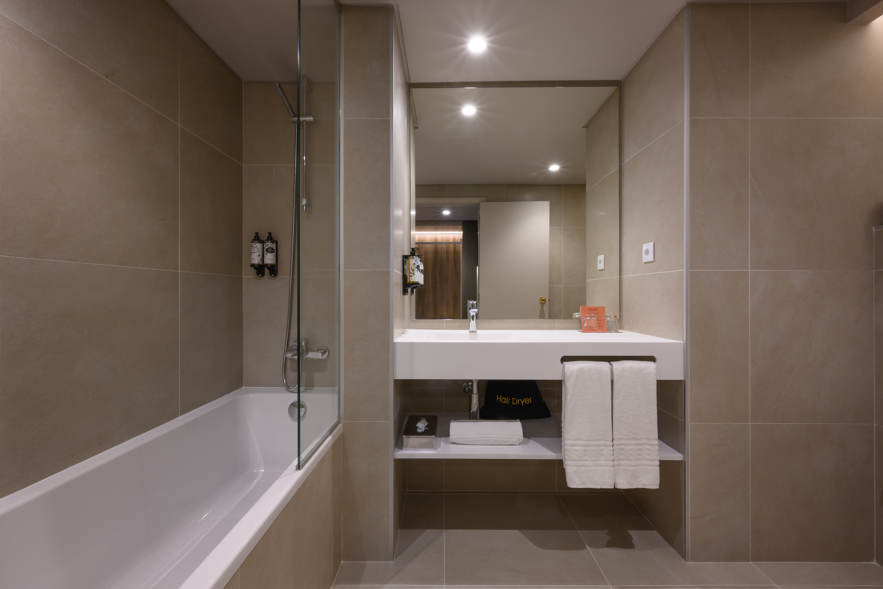 Modern hotel bathroom with bathtub, shower, vanity, mirror, and amenities.