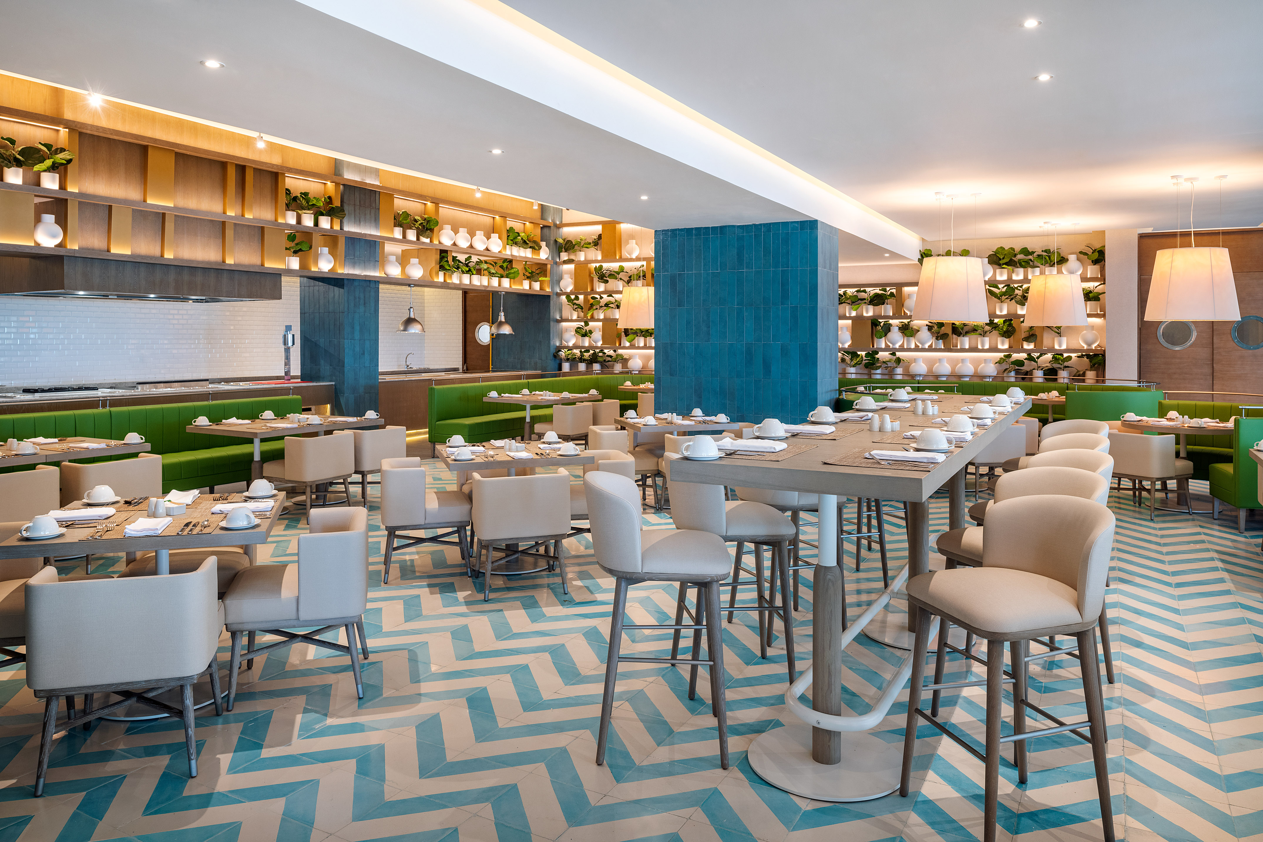 Modern restaurant dining area with green booths, beige chairs, and blue chevron floor.