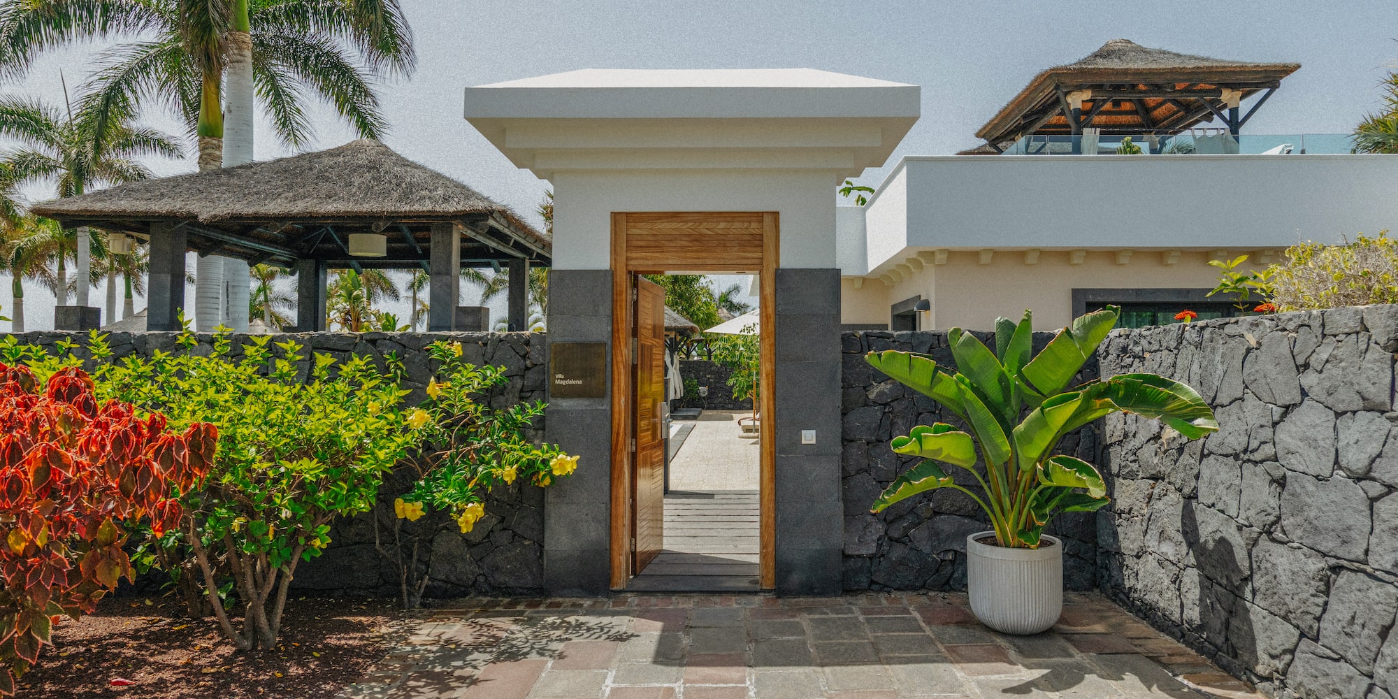 Villa Magdalena entrance gate with tropical garden, stone wall, and palm trees.